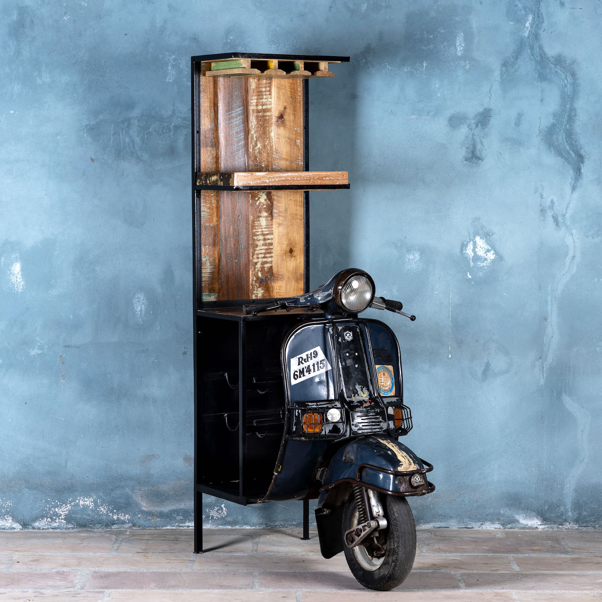 Side image of a high bar table featuring the front half of a vintage Bajaj scooter, with tall wooden shelving and an industrial metal frame, designed for stylish bar storage.