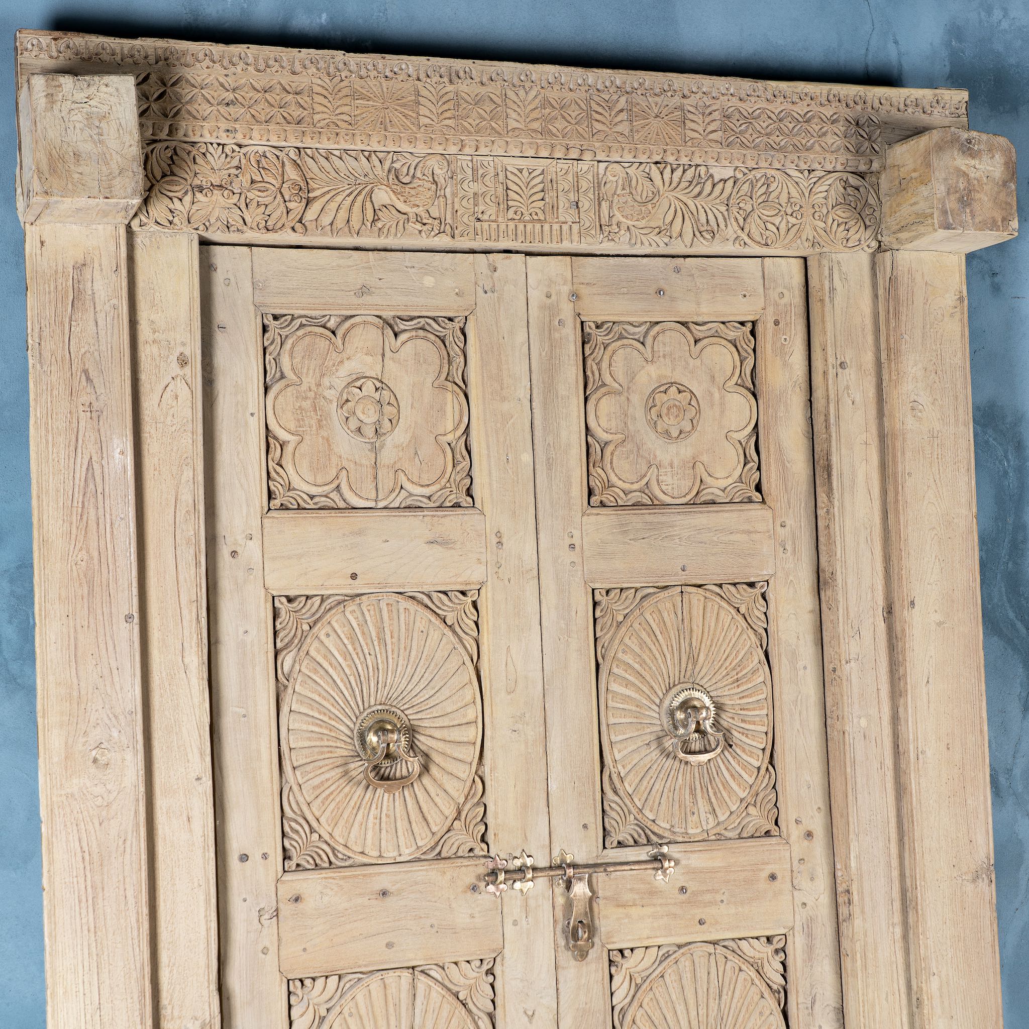 Close up image of a antique Indian door Akshara in reclaimed teak with brass locks, hand-carved details, extended frame, unique furniture and vintage wall panels, 148 × 30 × 225 cm.