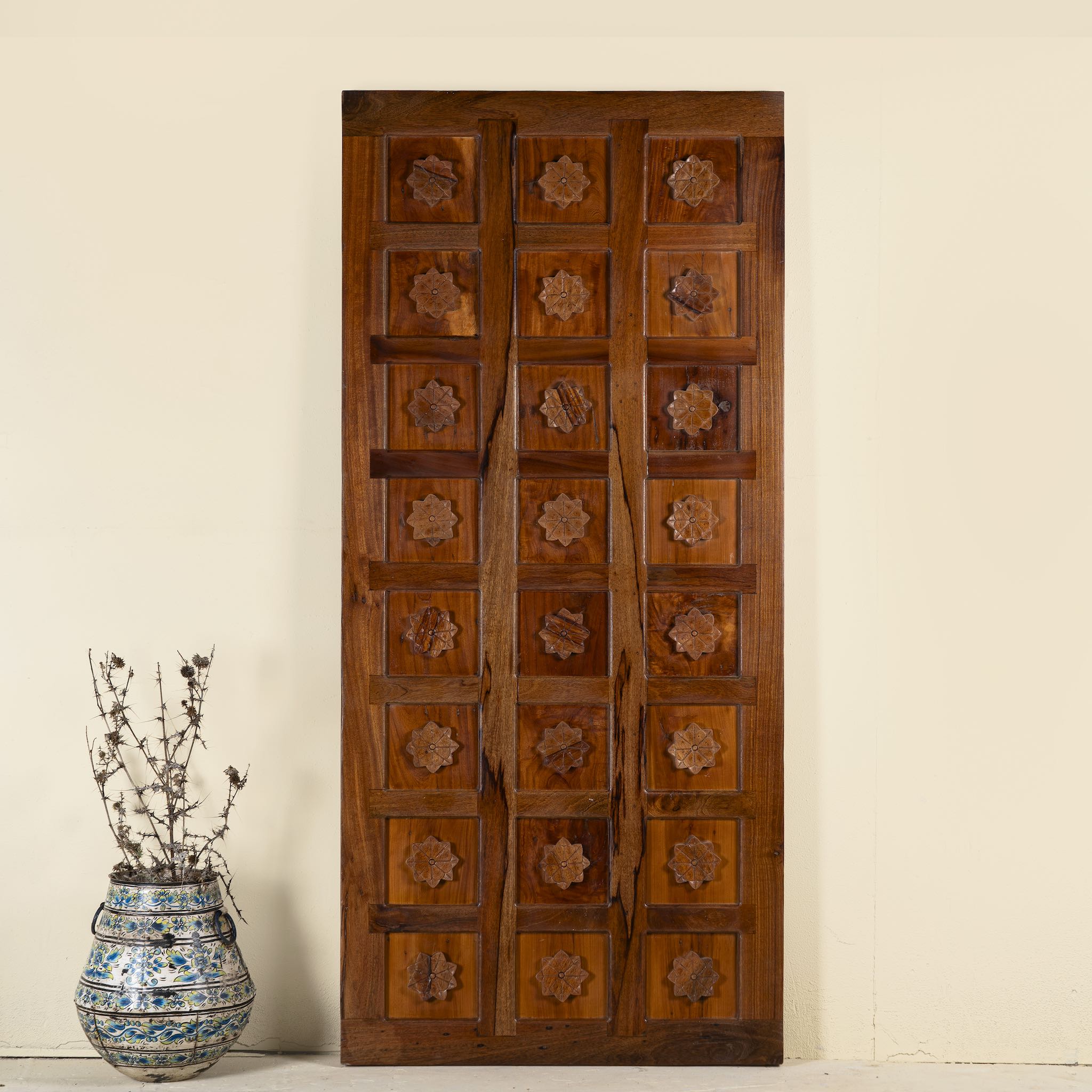 Hand-carved sliding door panel made from reclaimed wood, featuring symmetrical floral motifs in square reliefs for a warm, artisanal statement piece.