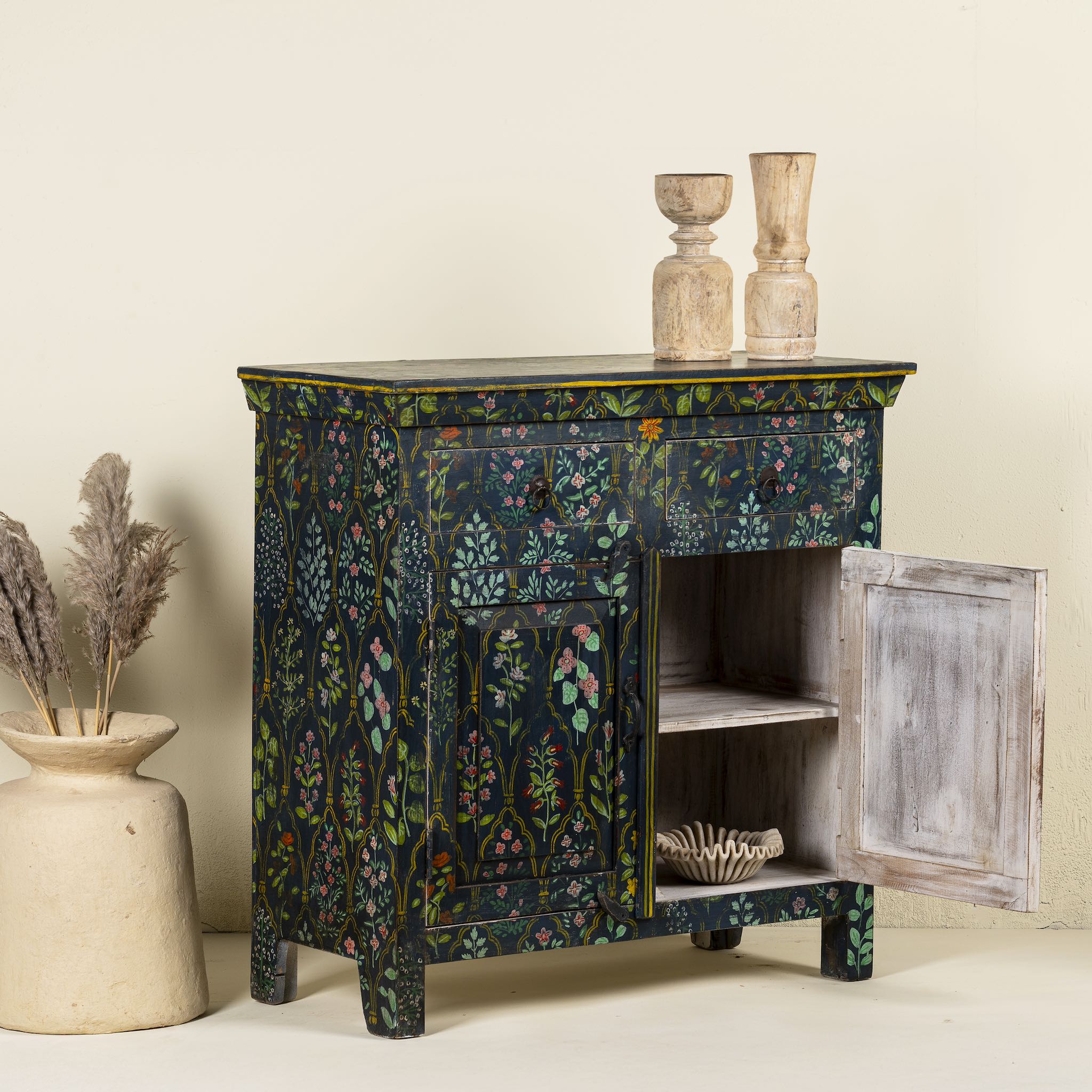 Side angle image with open door of a hand painted cupboard made from recycled wood with floral motifs, two drawers and two doors, 90 × 90 × 40 cm.
