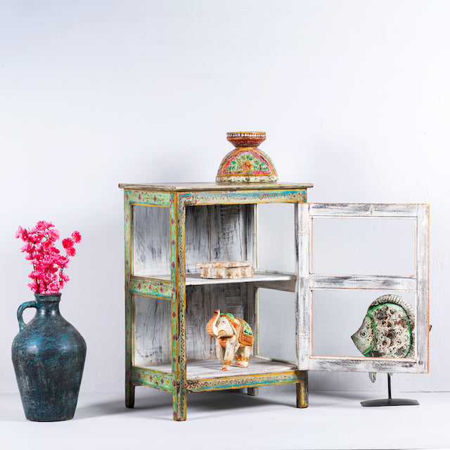 Side angle image wit open door of a vintage display cabinet in recycled wood with hand-painted decorative panels and glass display doors, 57 × 41 × 80 cm.