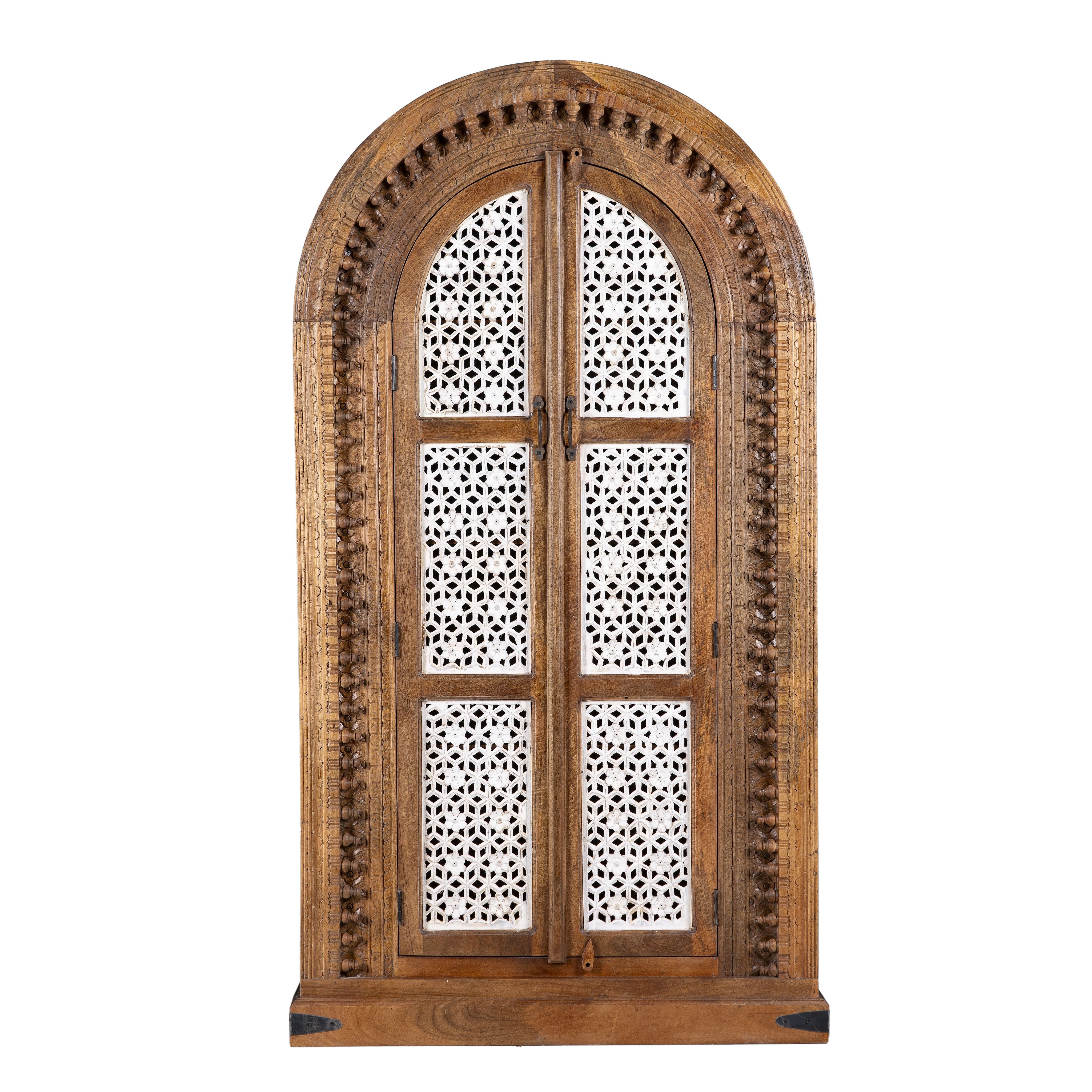 White background image of a handcrafted carved wooden wardrobe in half-round design with whitewashed lattice panels – bedroom furniture with Mediterranean flair and artistic detail.