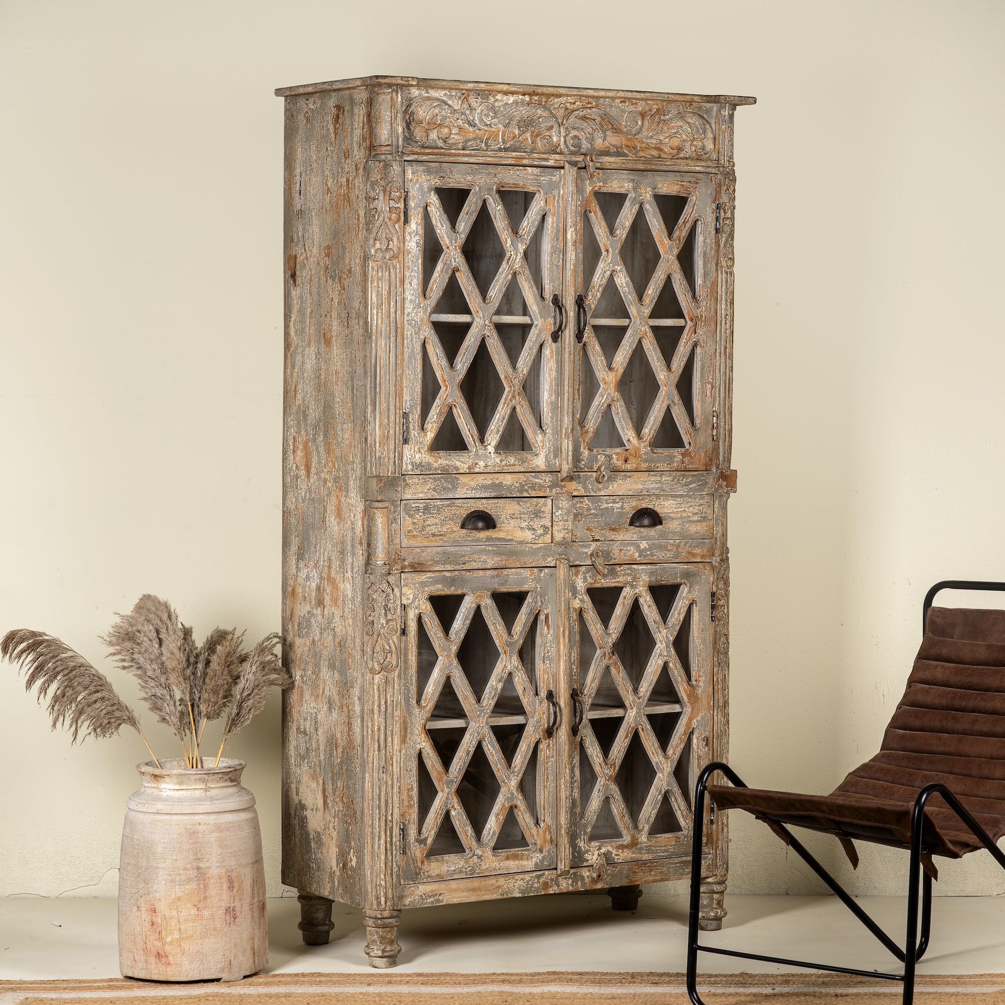 Side angle image of a vintage display cabinet made from solid mango wood with glass doors and shelving – handcrafted Ibiza-style showcase with carved details.