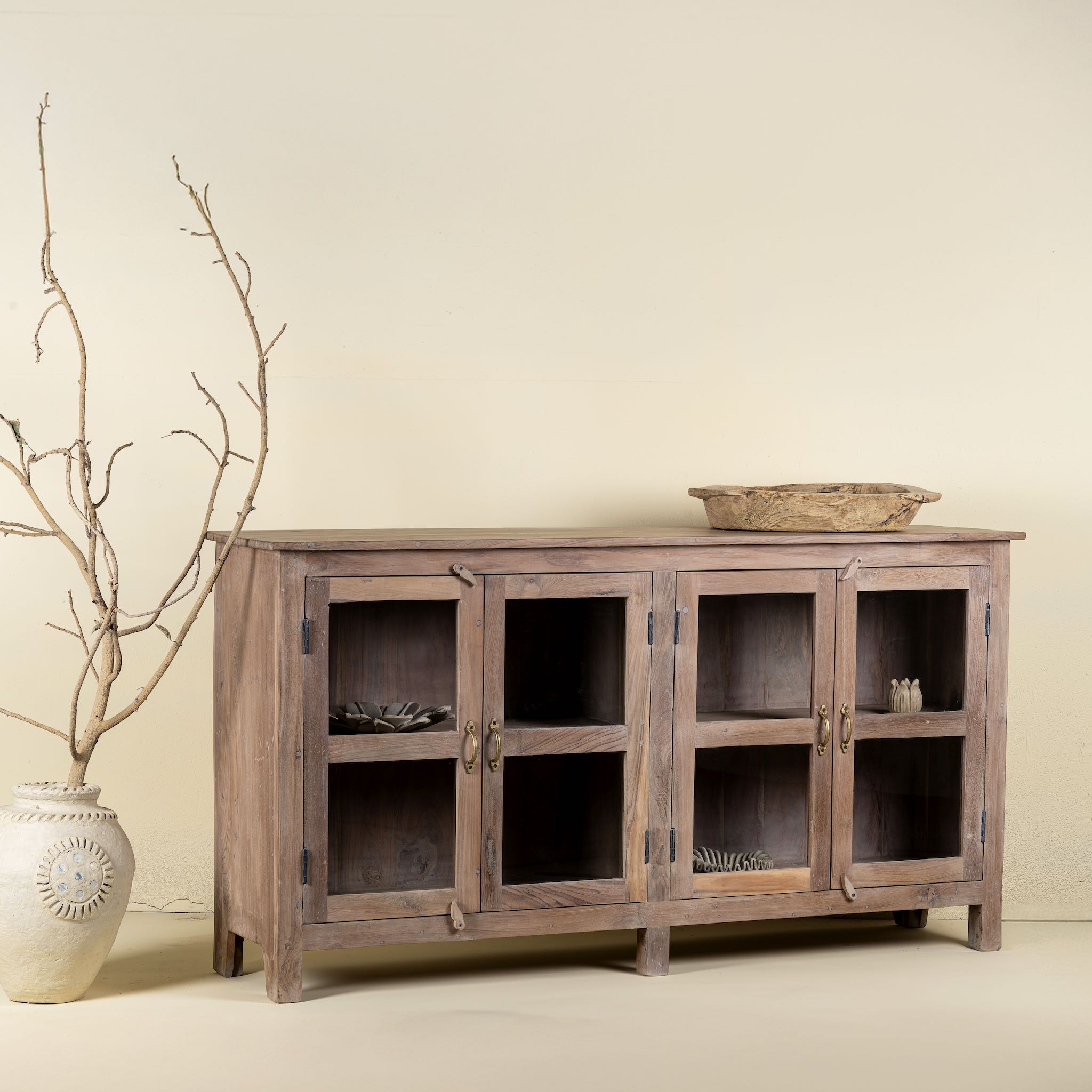 Side angle image of a reclaimed wood dresser with four glass doors, teak wood showcase cabinet with brass handles and wooden latches, 170 × 40 × 90 cm.