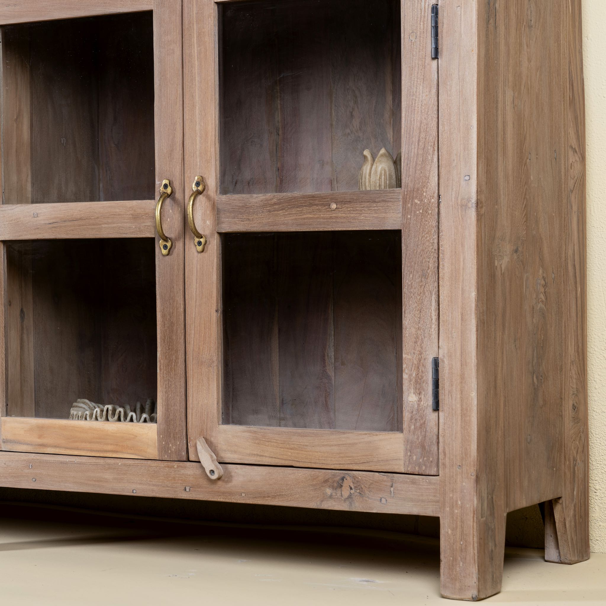 Close up image of the leg of a reclaimed wood dresser with four glass doors, teak wood showcase cabinet with brass handles and wooden latches, 170 × 40 × 90 cm.