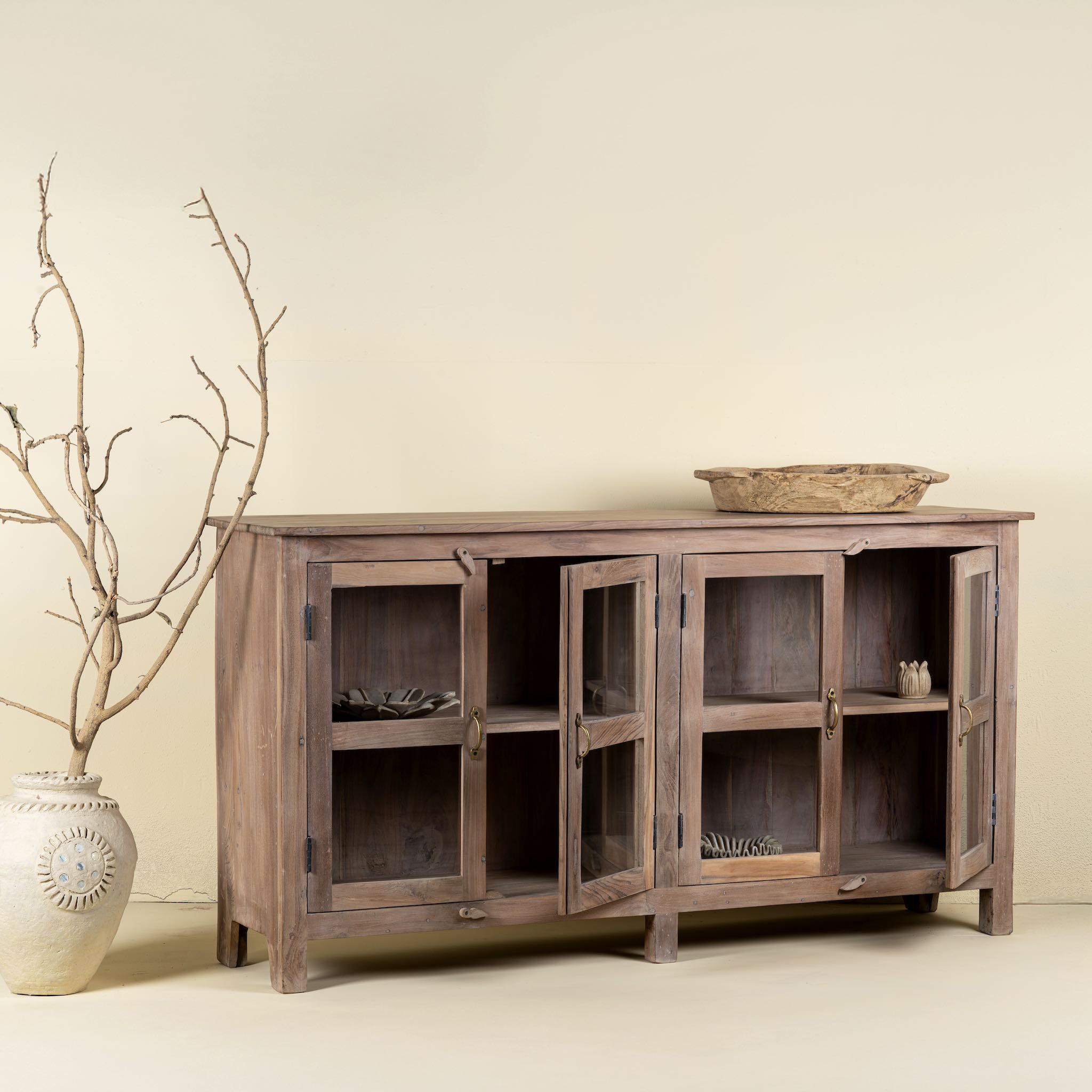 Side angle image with open doors of a reclaimed wood dresser with four glass doors, teak wood showcase cabinet with brass handles and wooden latches, 170 × 40 × 90 cm.