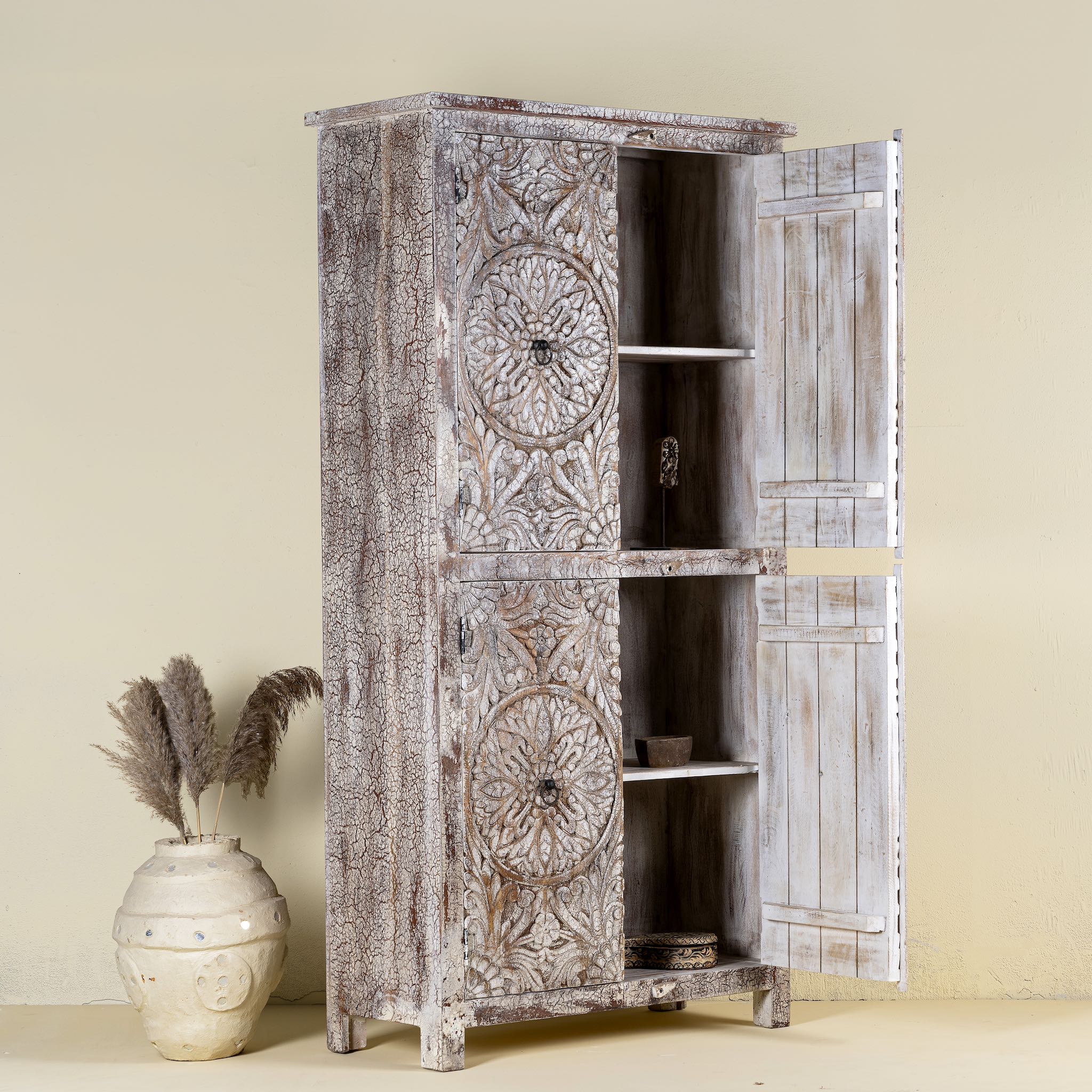 Open door view of a hand-carved acacia wood wardrobe with floral detailing and distressed finish – vintage living room furniture with artisan craftsmanship.