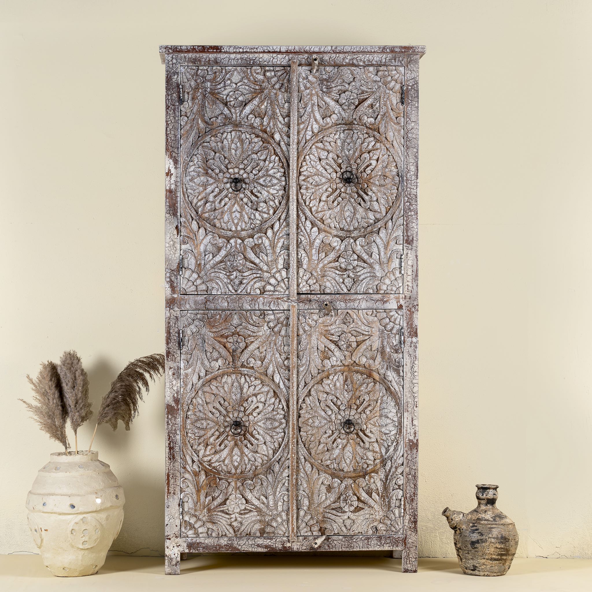 Front view of a hand-carved acacia wood wardrobe with floral detailing and distressed finish – vintage living room furniture with artisan craftsmanship.