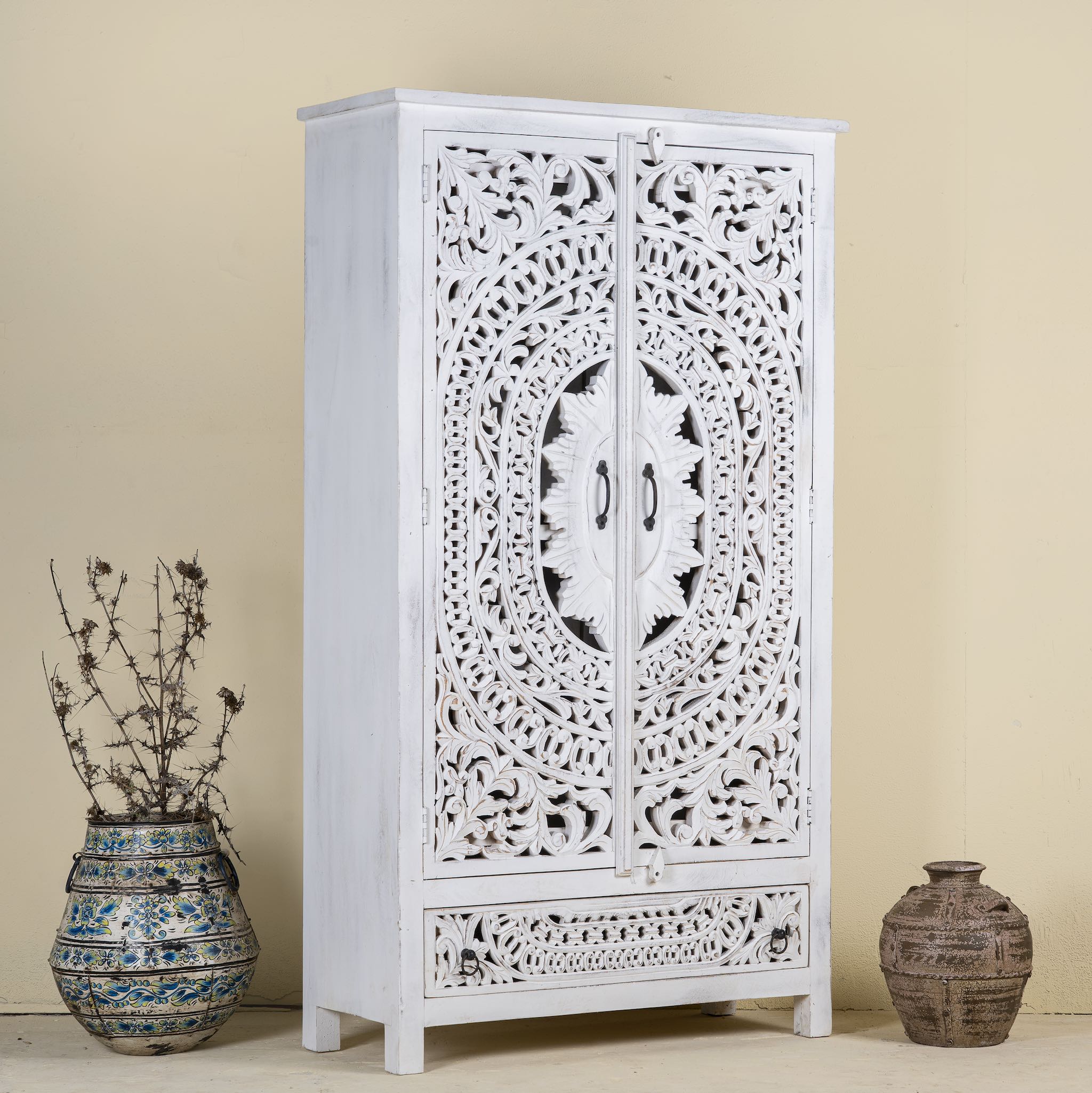 Side angle image of a hand-carved mango wood wardrobe with floral and geometric patterns and white-washed finish – carved wooden furniture for boho chic and Mediterranean-inspired interiors.
