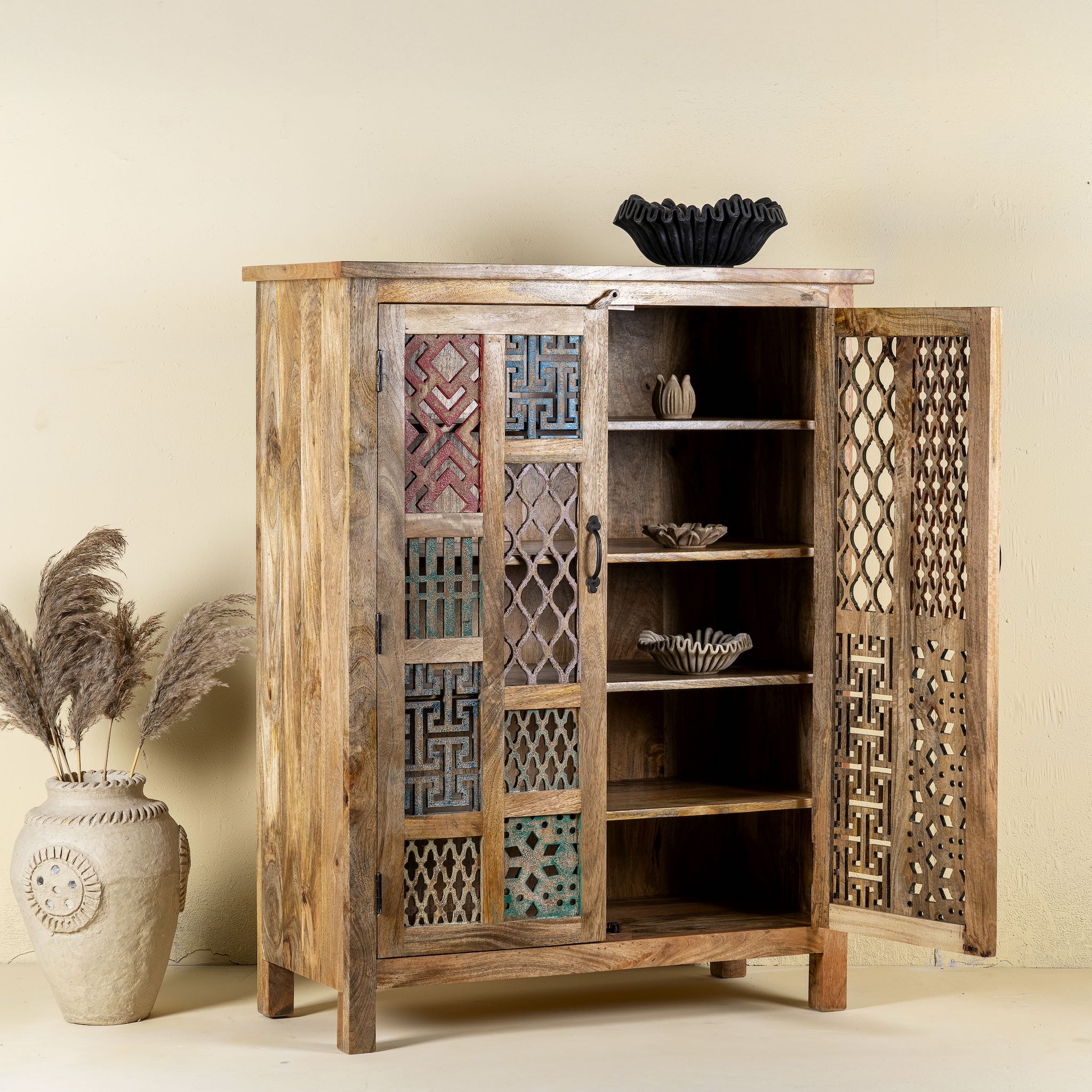 Side angle with open door image of a artisanal mango wood cabinet with hand-carved floral and geometric lattice doors, distressed finish; ideal for boho style interiors, 100 × 45 × 130 cm.