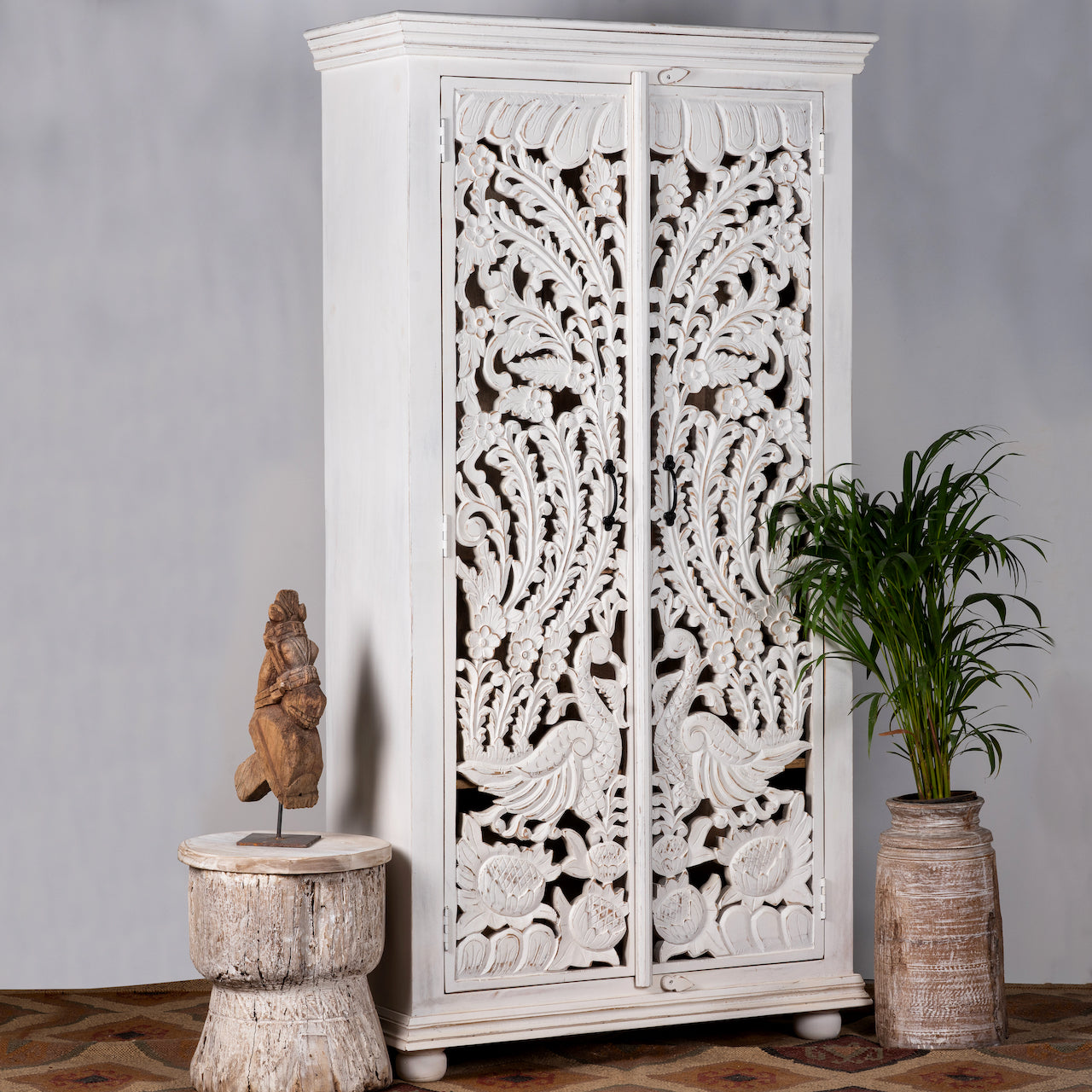 Side angle image of a hand-carved mango wood wardrobe with peacock and floral motifs, whitewashed finish; elegant wooden wardrobe and mango wood furniture, 190 × 100 × 40 cm.