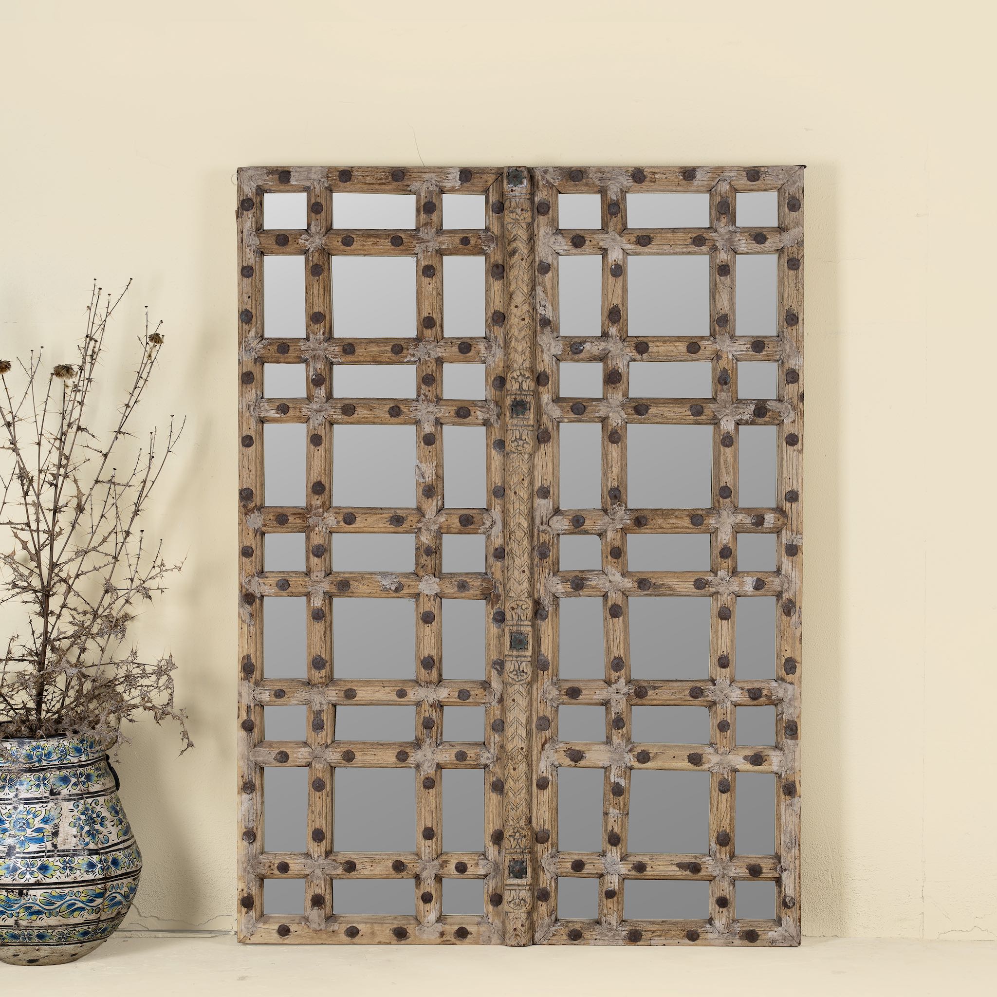 Statement wall mirror made from an old teak window frame with large square grid pattern, metal studs, and decorative center carving- a bold blend of rustic charm and historic craftsmanship.