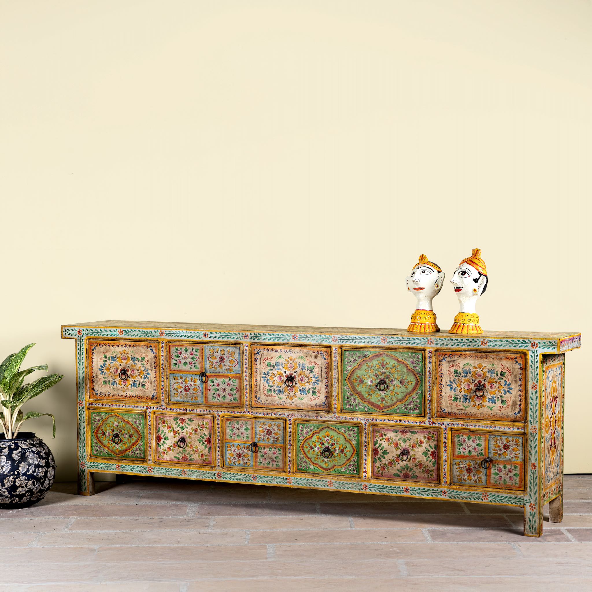 Side angle image of a hand painted mango wood chest of 11 drawers with floral motifs; artisanal mango wood furniture and hand painted furniture, 250 × 41 × 85 cm.