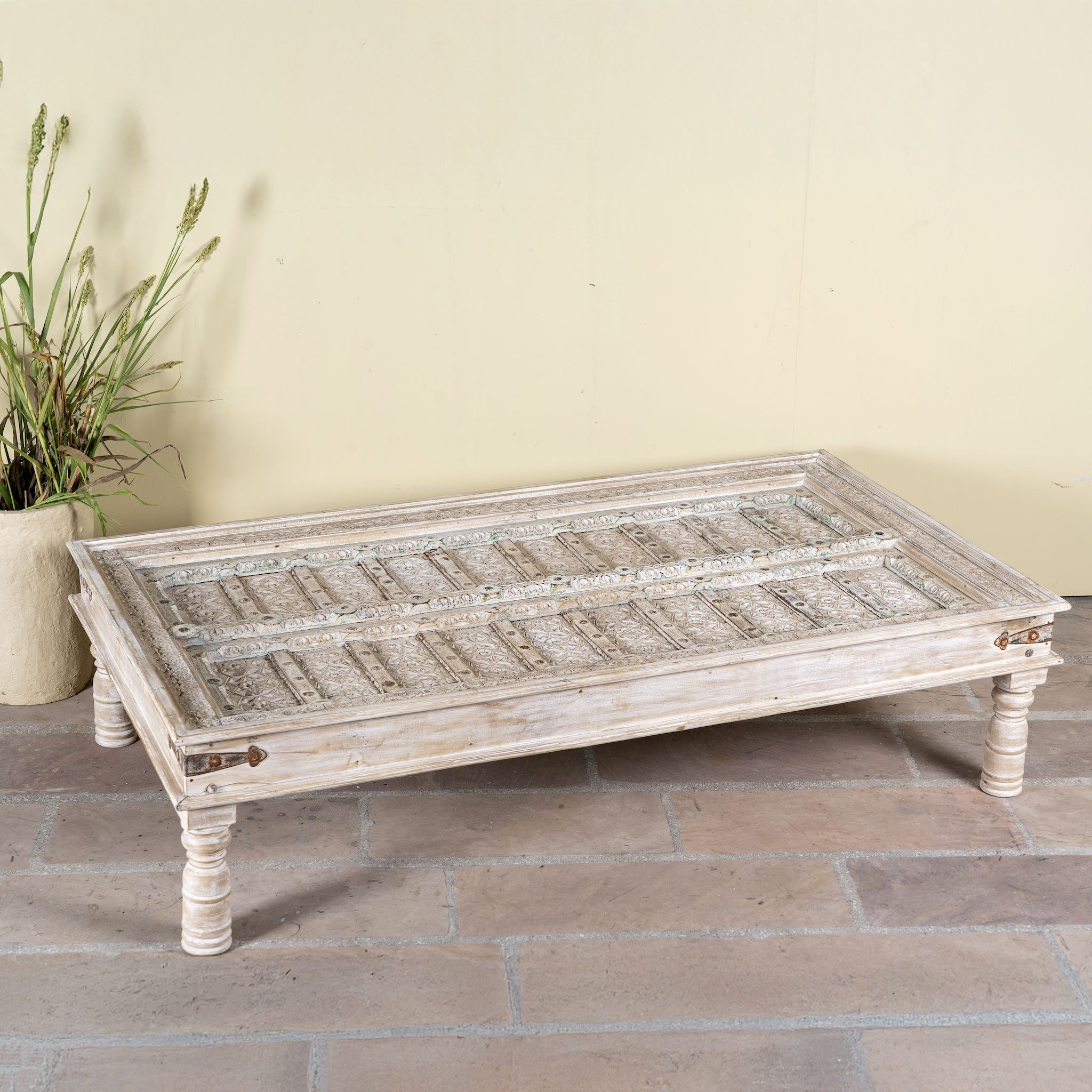 Lifestyle image of a white washed old door coffee table made of antique teak wood; handcrafted Indian coffee table, 183 × 100 × 45 cm.