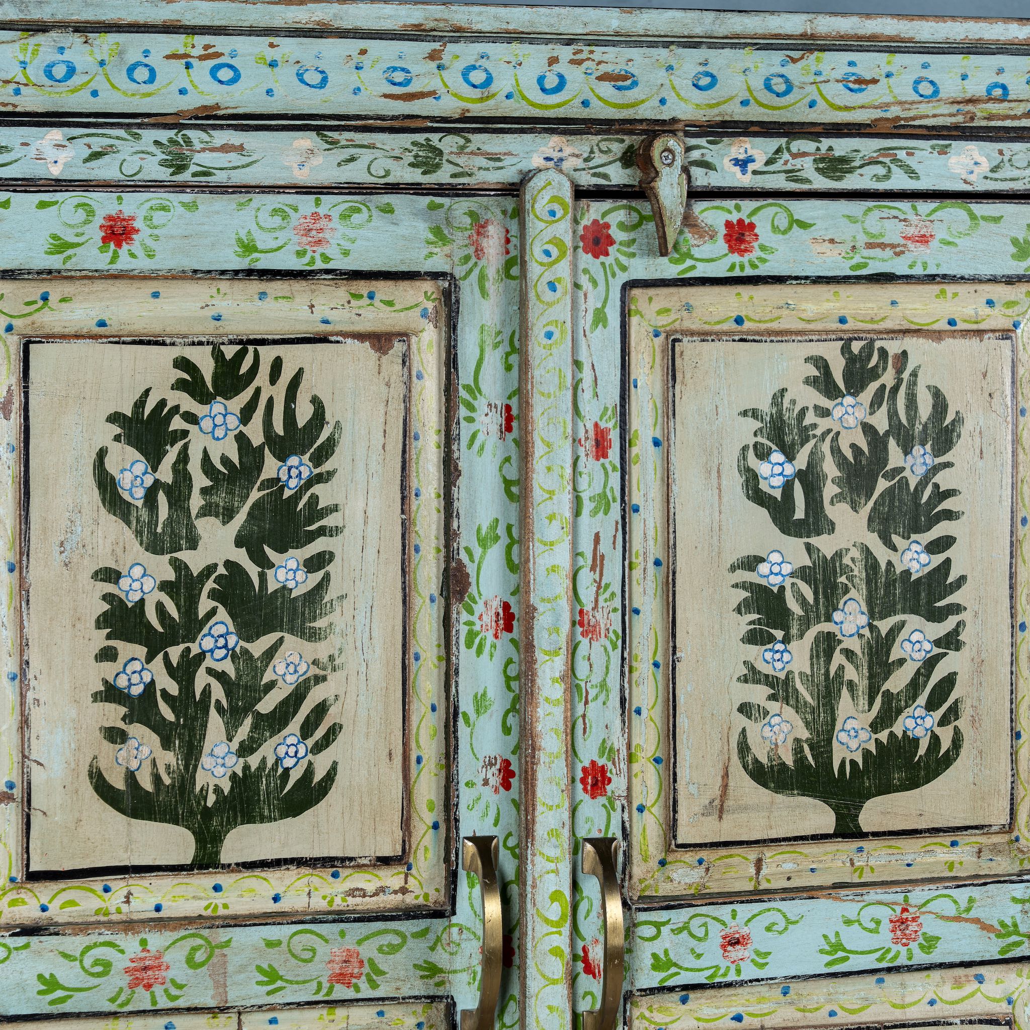 Close up picture of a vintage cabinet made from reclaimed wood, featuring hand-painted floral and tree motifs in vibrant green, red, and turquoise tones for a joyful, artistic touch.