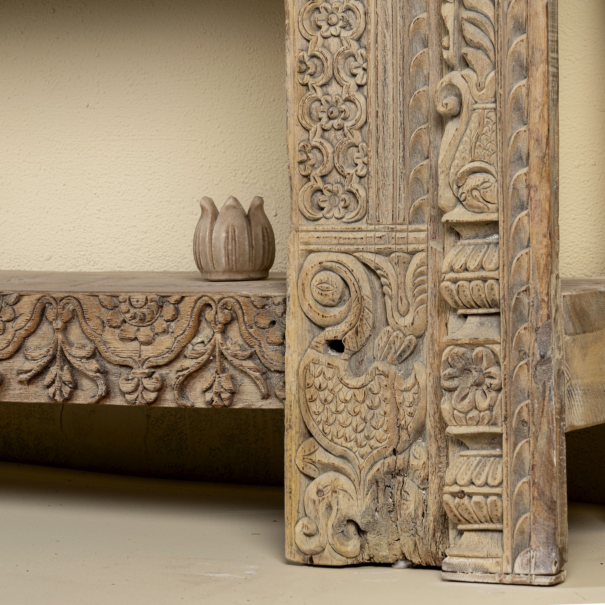 Close up image of a leg design of a ornate console table crafted from reclaimed teak wood and refurbished architectural elements, featuring intricate hand-carved detailing with floral and geometric motifs, showcasing a vintage artisanal aesthetic.