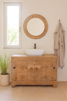 Bathroom with wooden vanity, round mirror, and plant