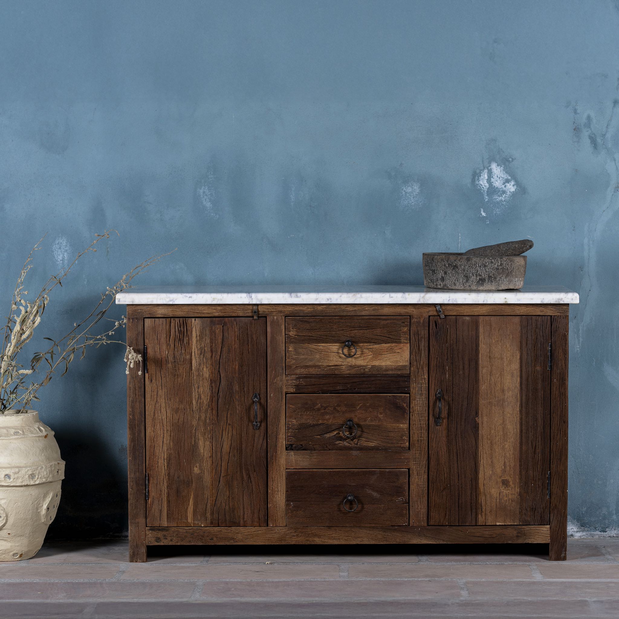 Front view of a driftwood sideboard with iron handles, 3 drawers and 2 doors and a slidable marble top in a maritime scene.