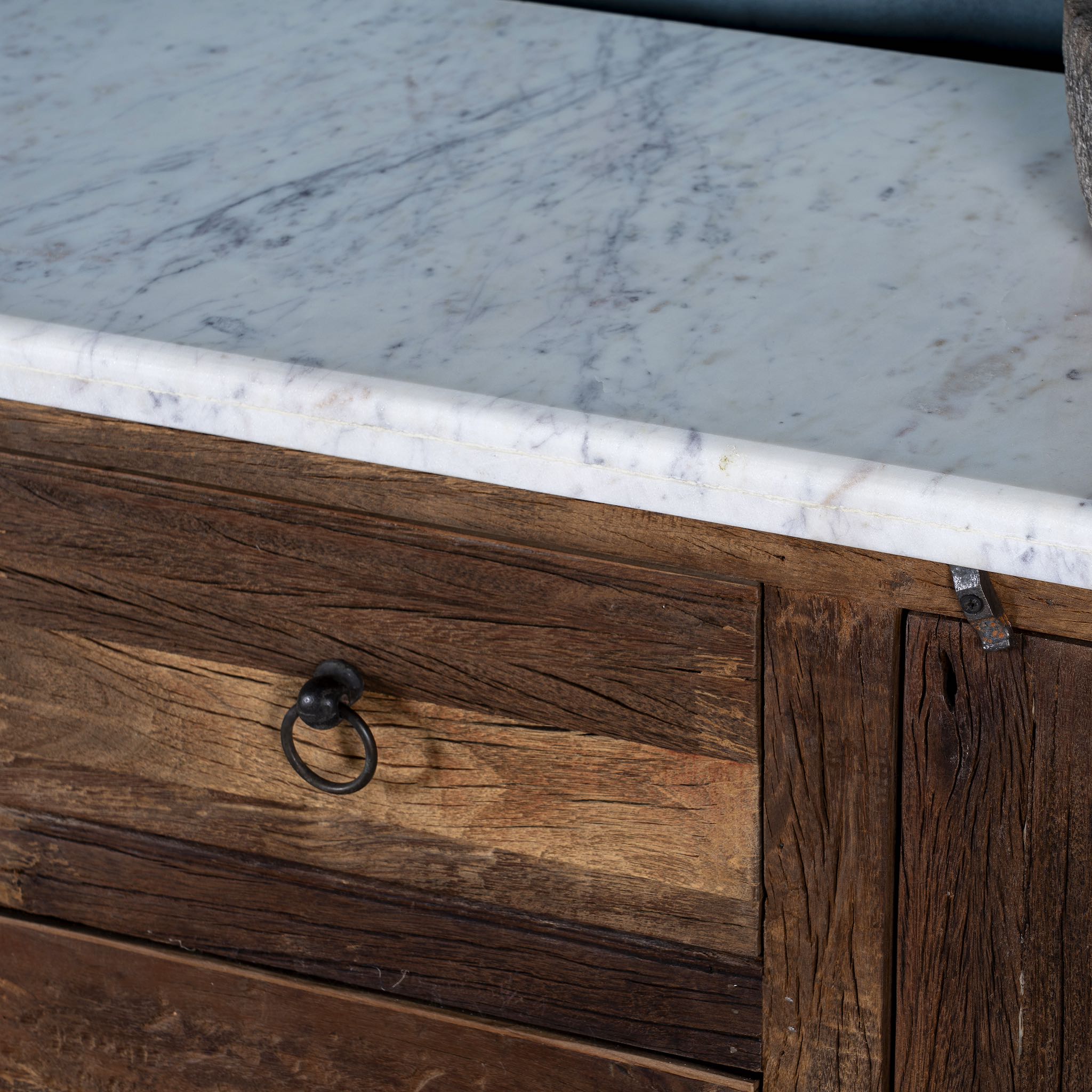 Close up picture of a driftwood sideboard with iron handles, 3 drawers and 2 doors and a slidable marble top in a maritime scene.