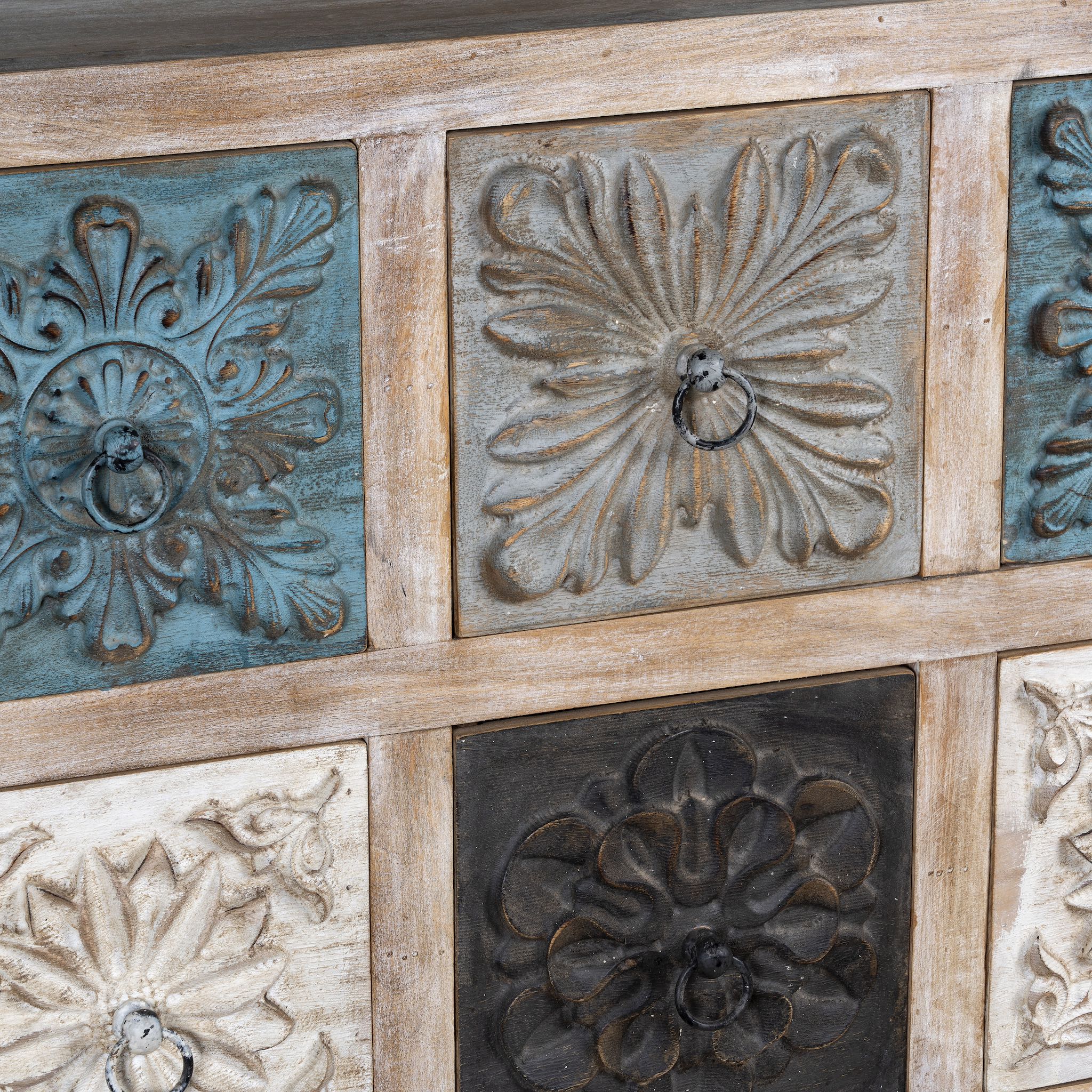 Close up image of a mango wood chest of drawers Hansika with nine hand-carved floral drawer fronts in soft bohemian colours. A unique carved sideboard combining artisan design with versatile storage.