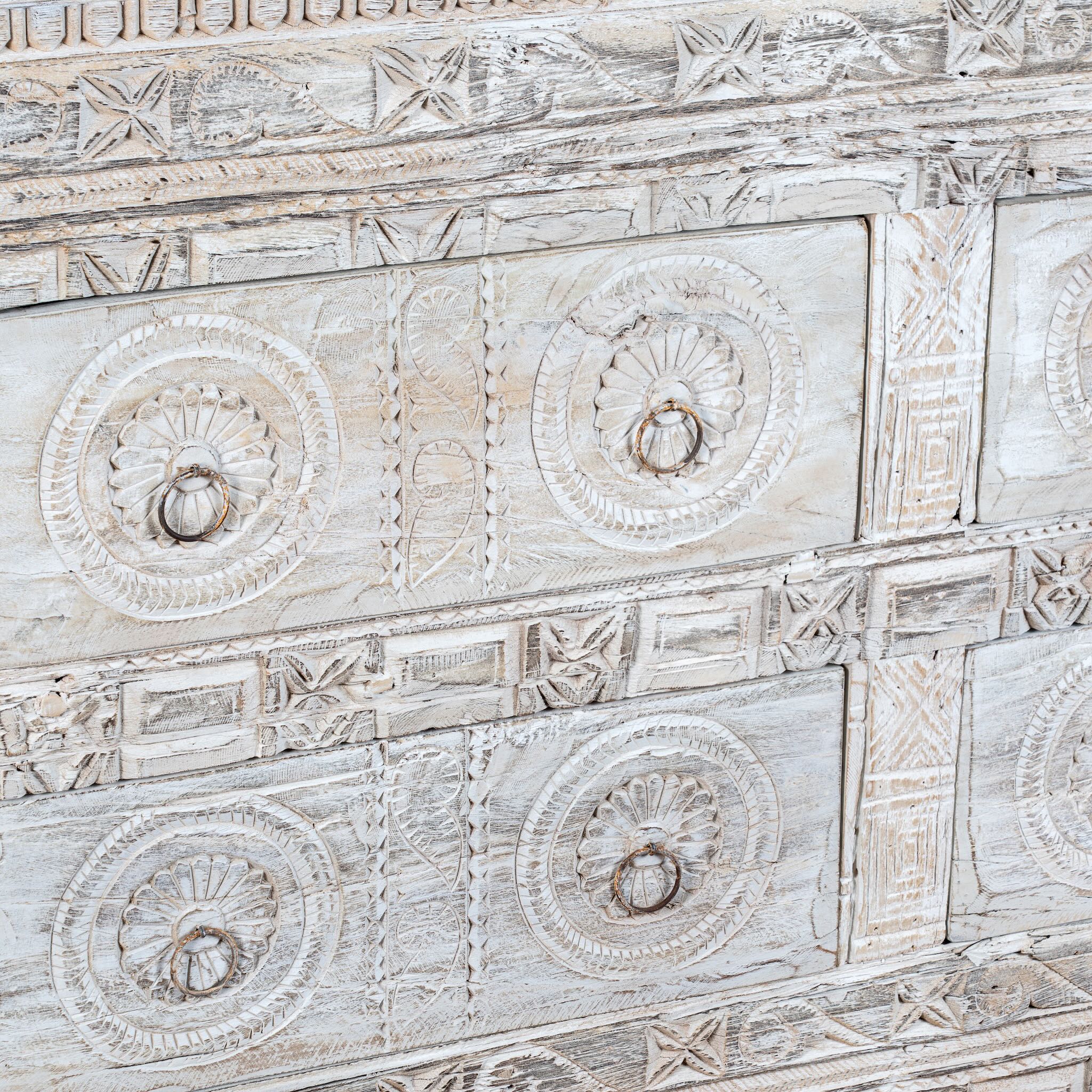 Close up image of a handcrafted chest of drawers Hemali made from reclaimed wood, featuring four carved drawers with circular motifs and a whitewashed finish. A rustic, sustainable furniture piece with soft texture and elegant detailing.