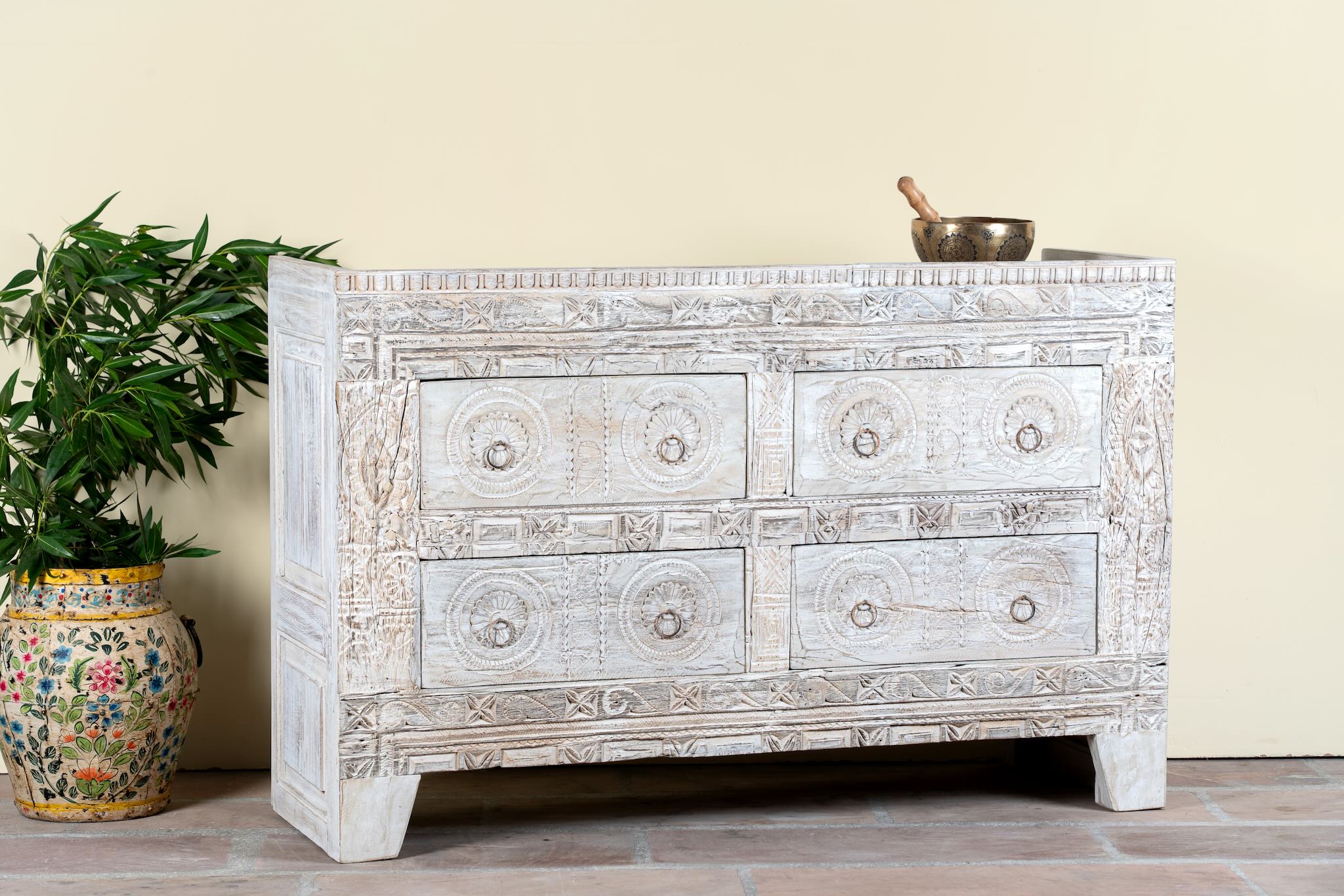 Side angle image of a handcrafted chest of drawers Hemali made from reclaimed wood, featuring four carved drawers with circular motifs and a whitewashed finish. A rustic, sustainable furniture piece with soft texture and elegant detailing.