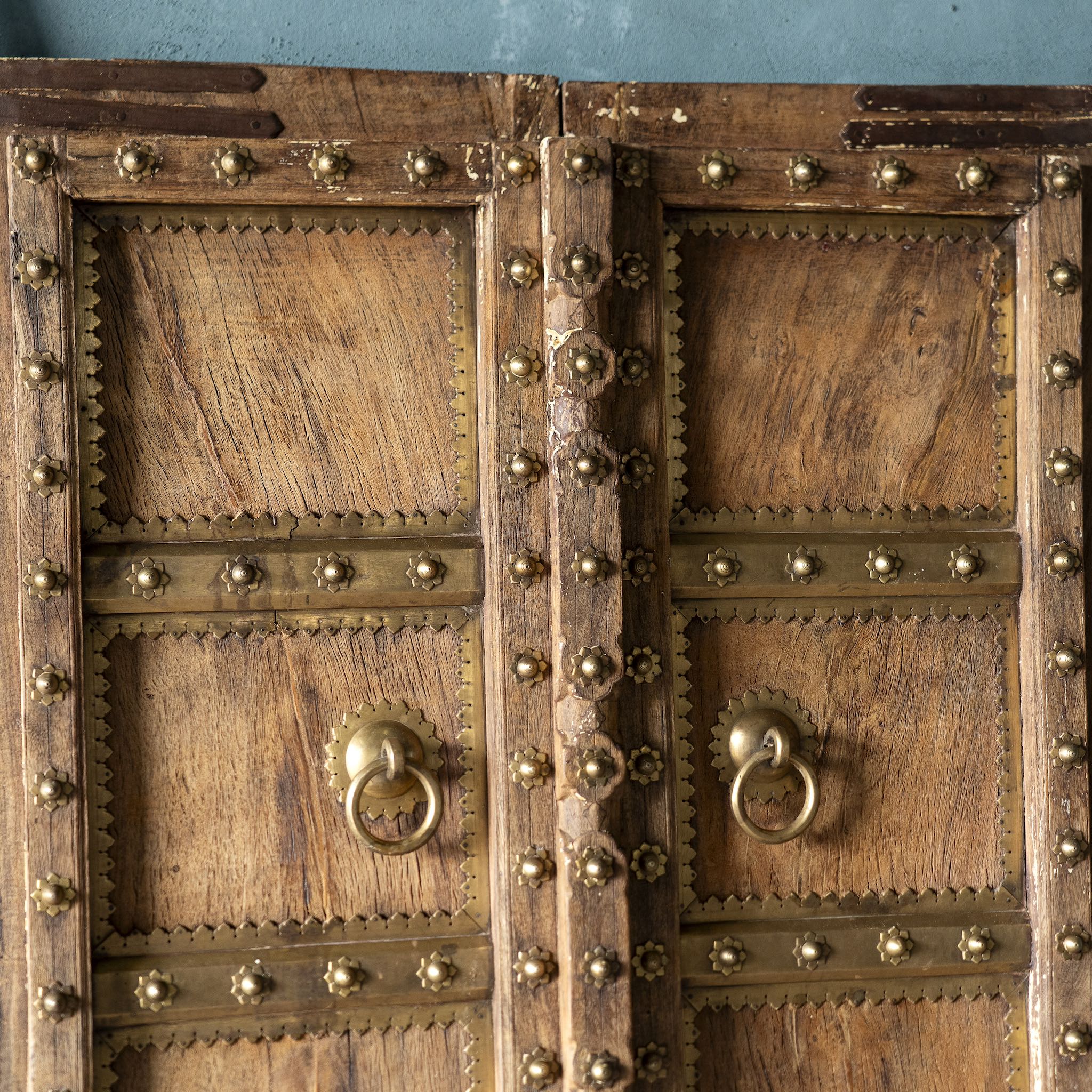 Close up of an antique Indian temple door made of old teak with original brass fittings, locks, and ring handles, featuring a richly aged patina from a historic Jain temple.