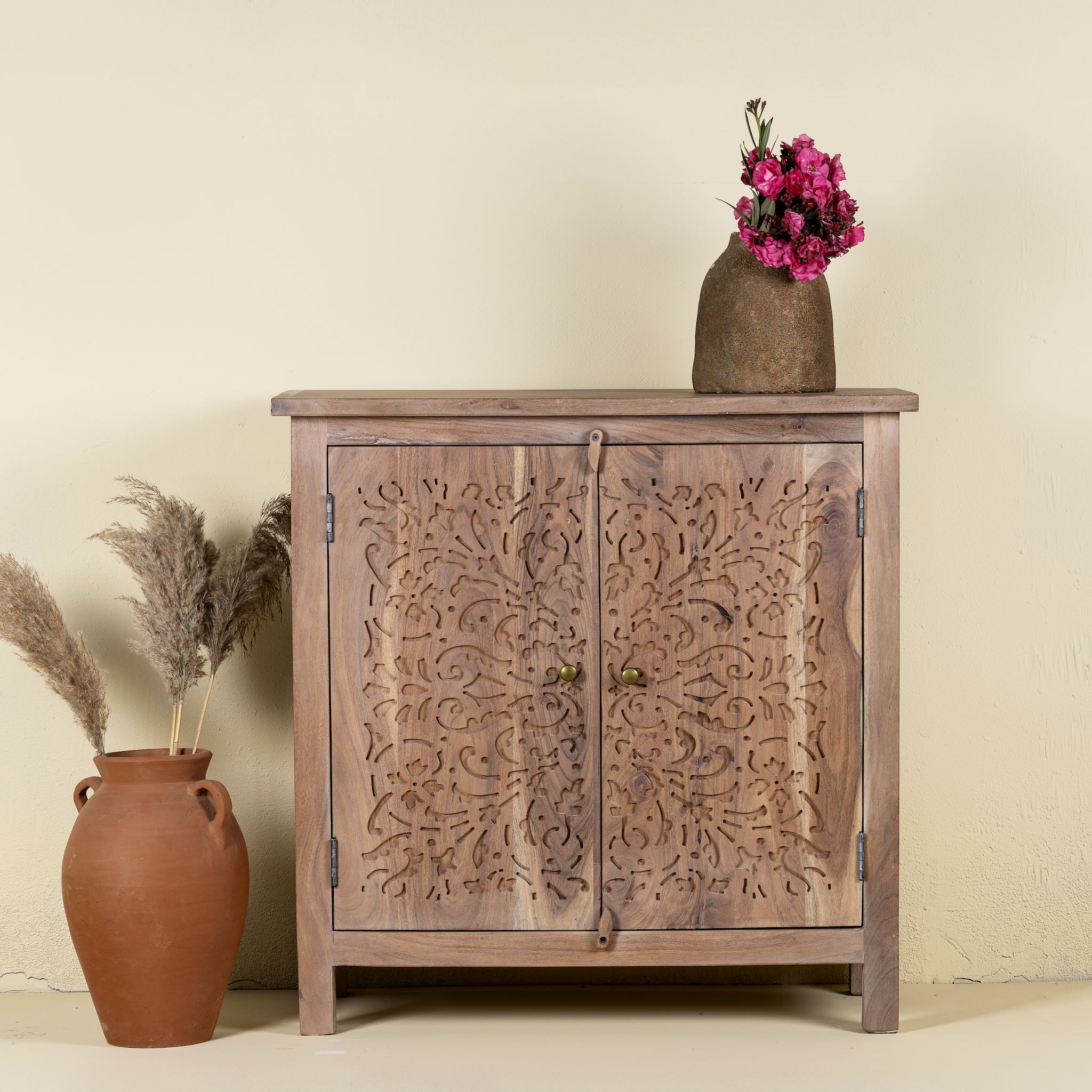 Carved acacia wood cupboard with floral cutout doors and brass knobs, 90 × 40 × 90 cm.