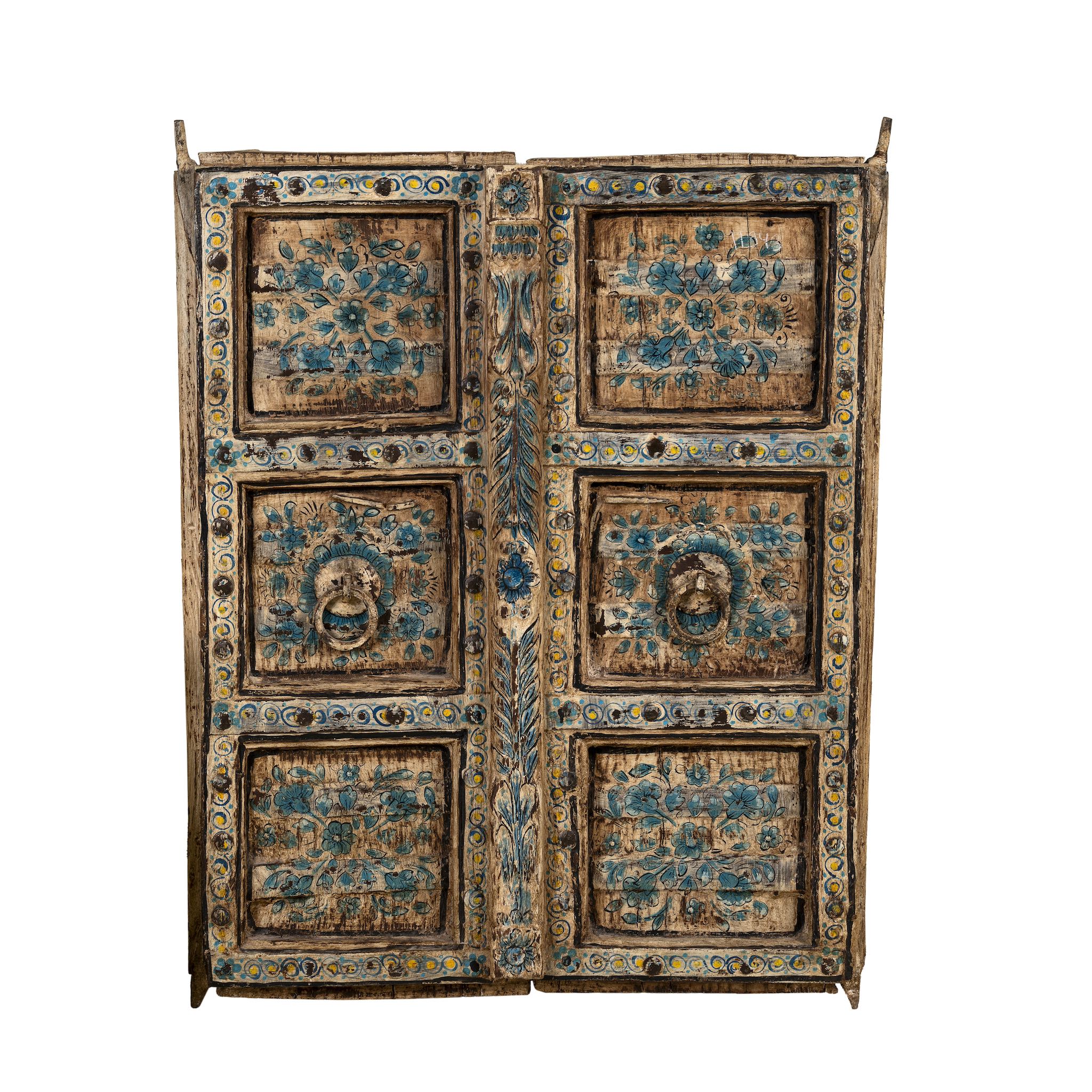 White background image of a antique wall panel made from an old teak wood window frame, featuring hand-painted blue floral motifs on a distressed natural wood background, with ornate yellow, white, and blue border accents and decorative metal ring pulls.
