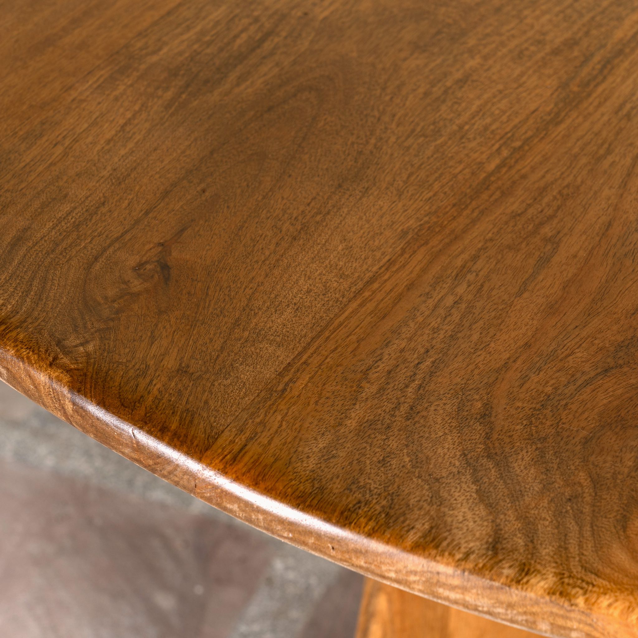 Close up image of a round mango wood dining table with natural grain and sturdy base; solid wooden dining table for dining rooms, 130 cm diameter × 100 cm height.