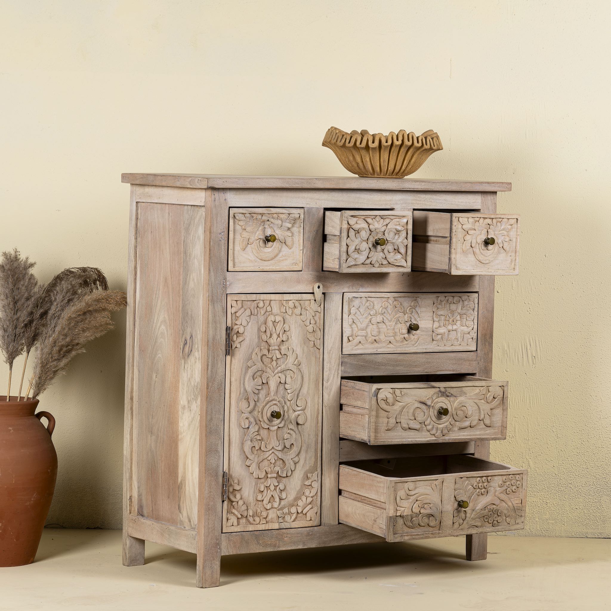 Open drawer view of a hand carved mango wood cupboard with 6 drawers and 1 door, iron fitted door knobs and floral carvings.