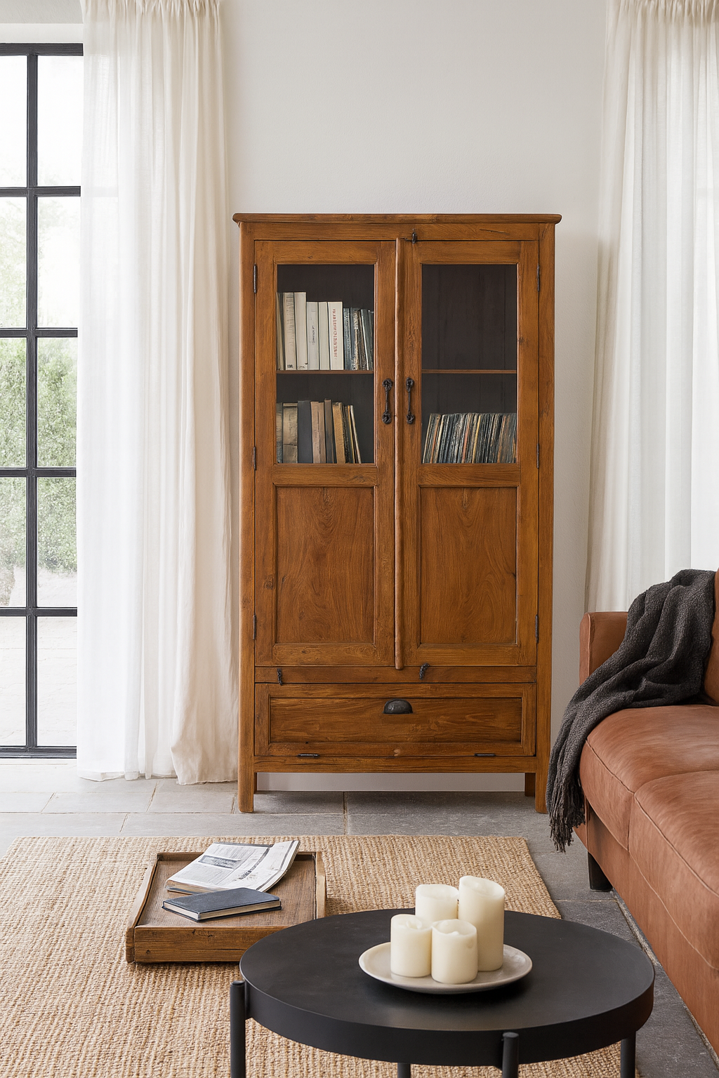 Lifestyle image of a tall reclaimed teak wood display cabinet with two glass doors and a bottom drawer – wooden display cabinet crafted as sustainable furniture with natural elegance.