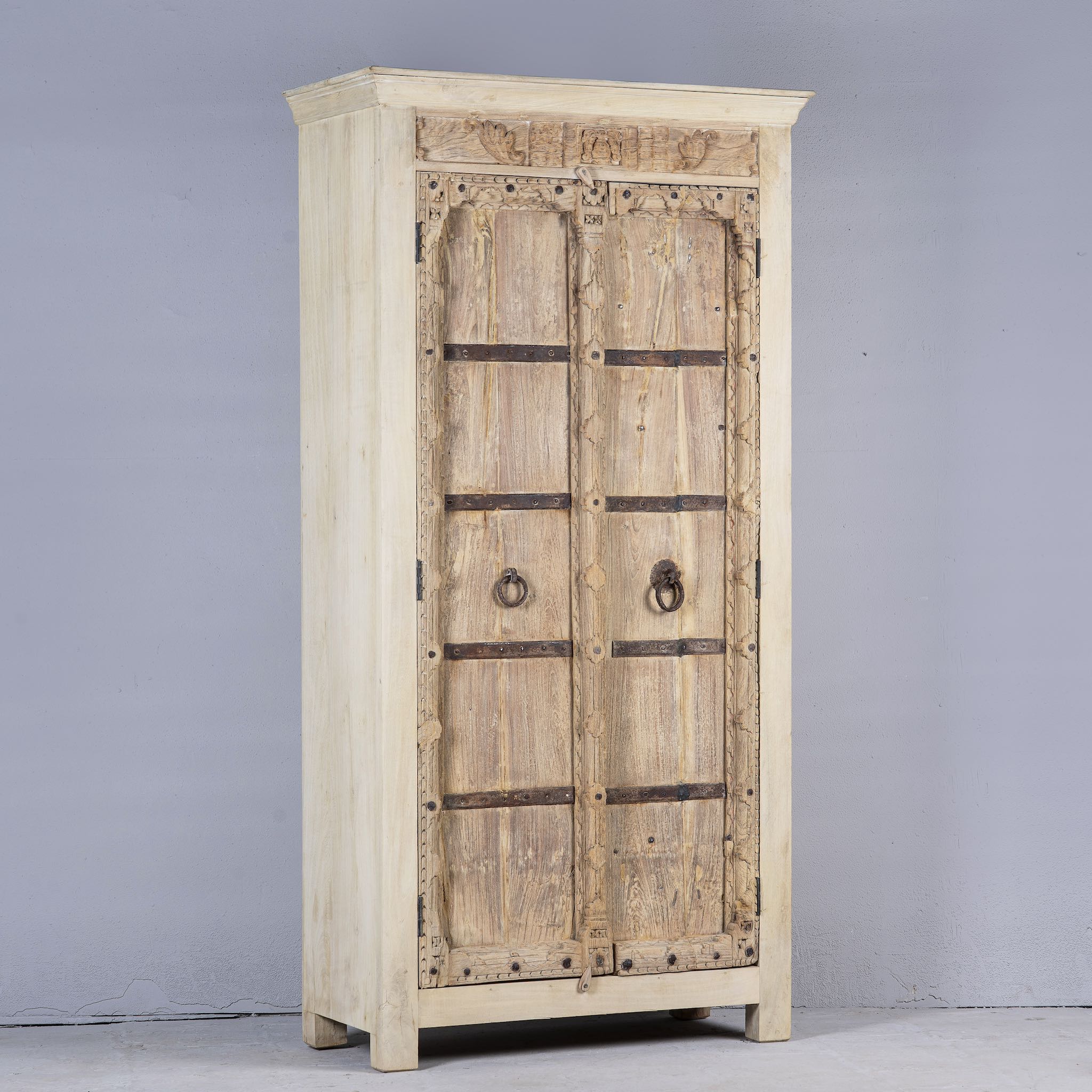 Side angle image of a rustic solid wood wardrobe featuring vintage reclaimed door panels with iron accents and ring pull handles.