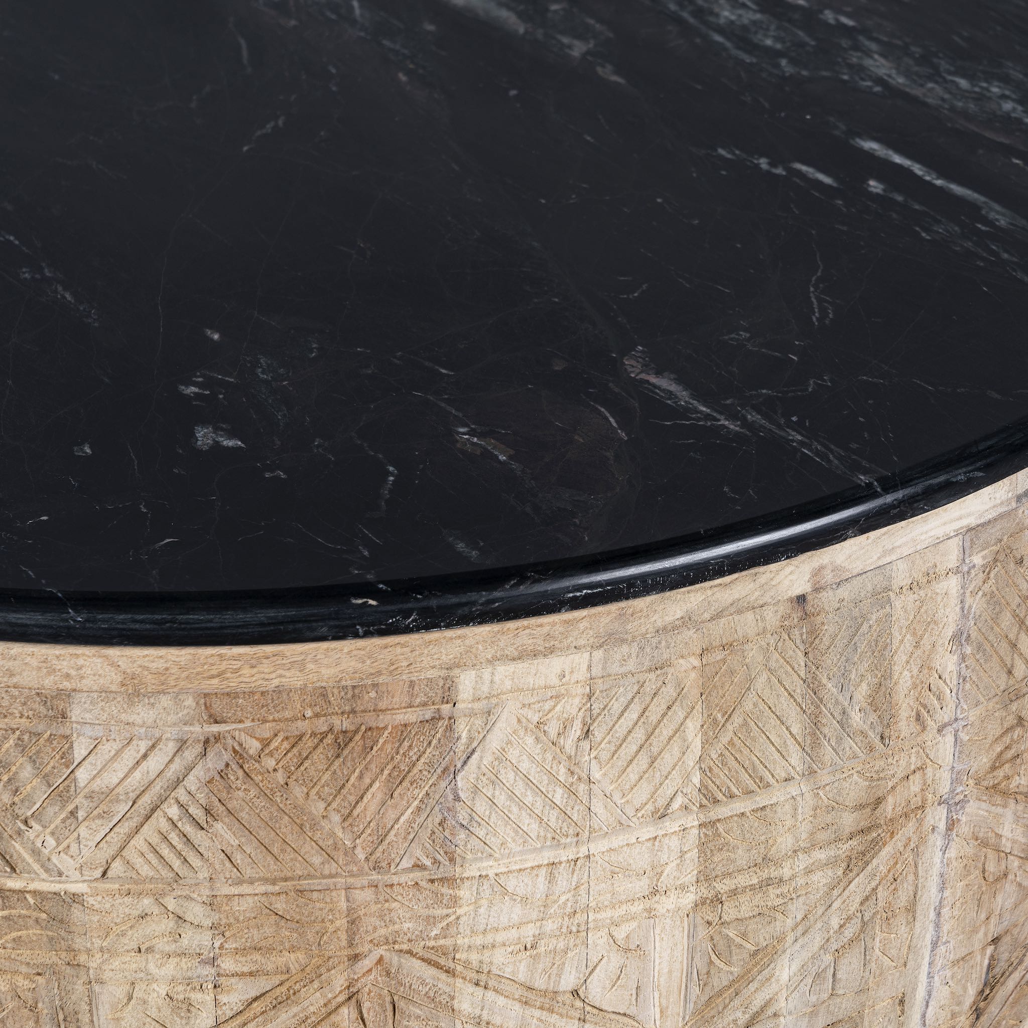 Close up view of a elegant round hand carved coffee table made of sustainable Mango wood with floral design and black marble top.