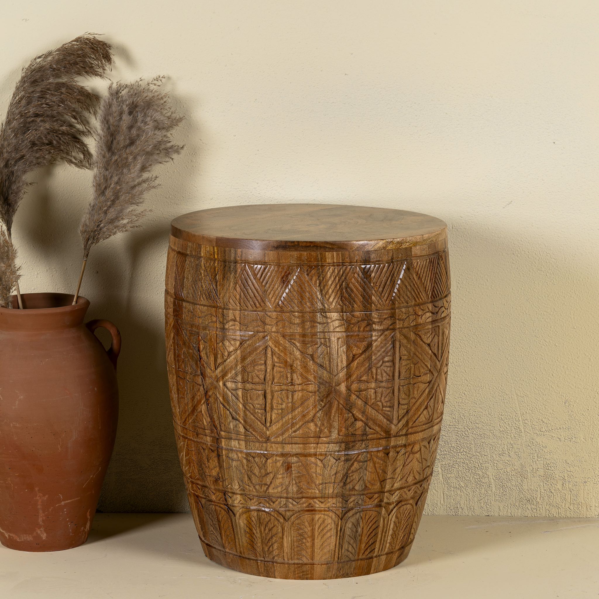 Front view of a round mango wood side table with hand carved floral and geometrical design.