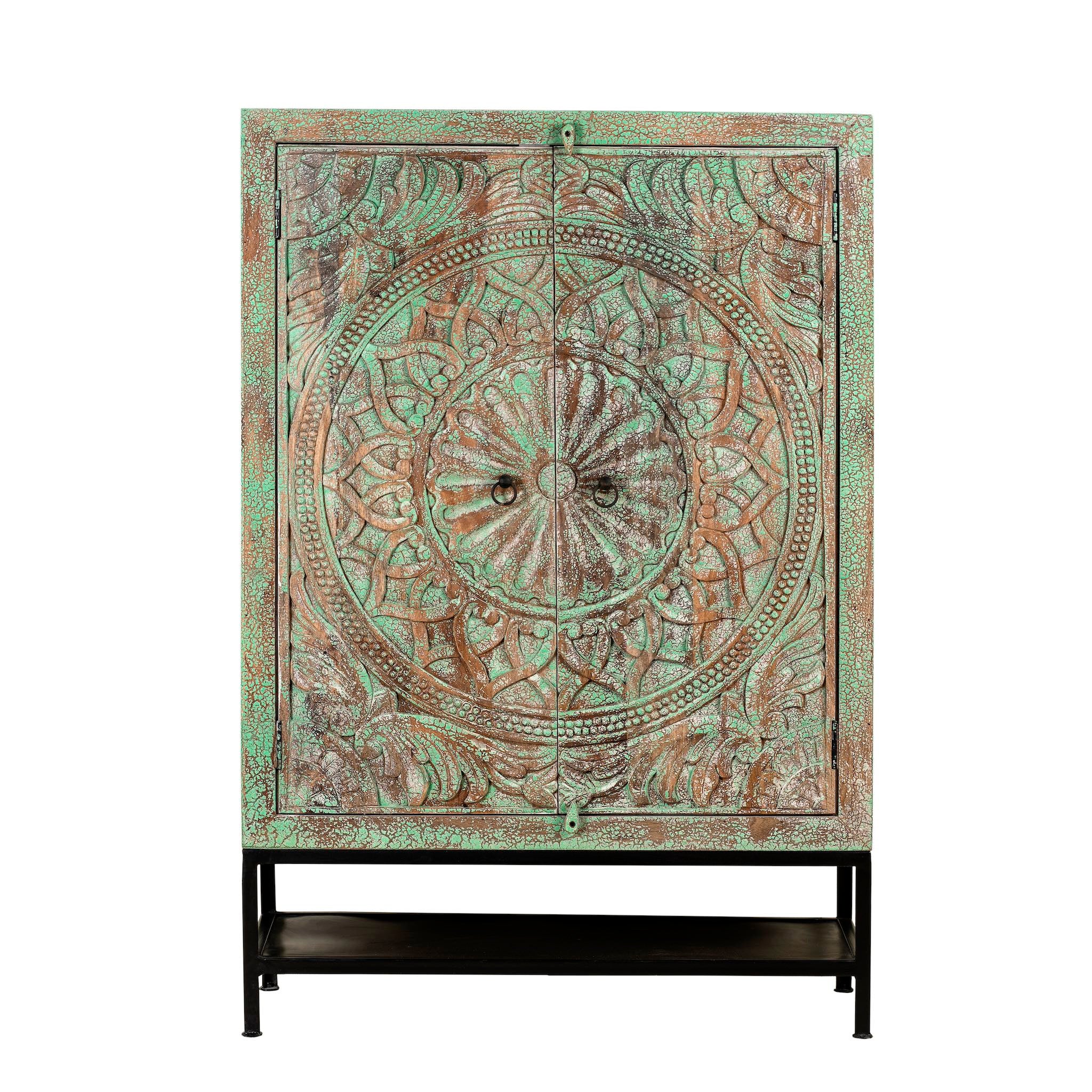 White background image of a carved mango wood cabinet with floral hand-carving, distressed green finish, iron stand, 100 × 40 × 150 cm.