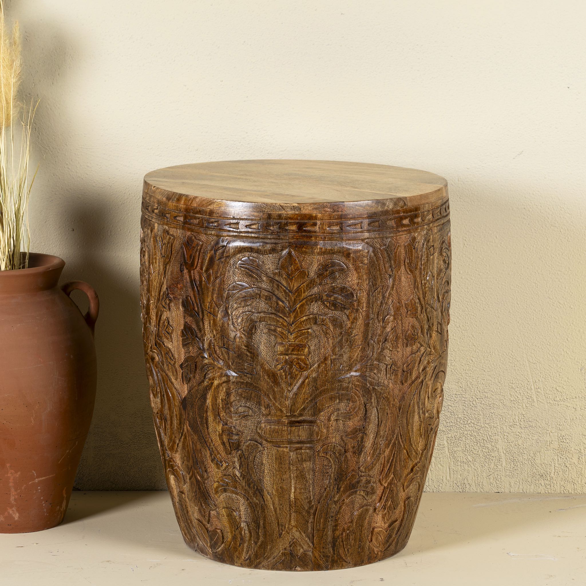 Front view of a round mango wood side table with hand carved floral design.