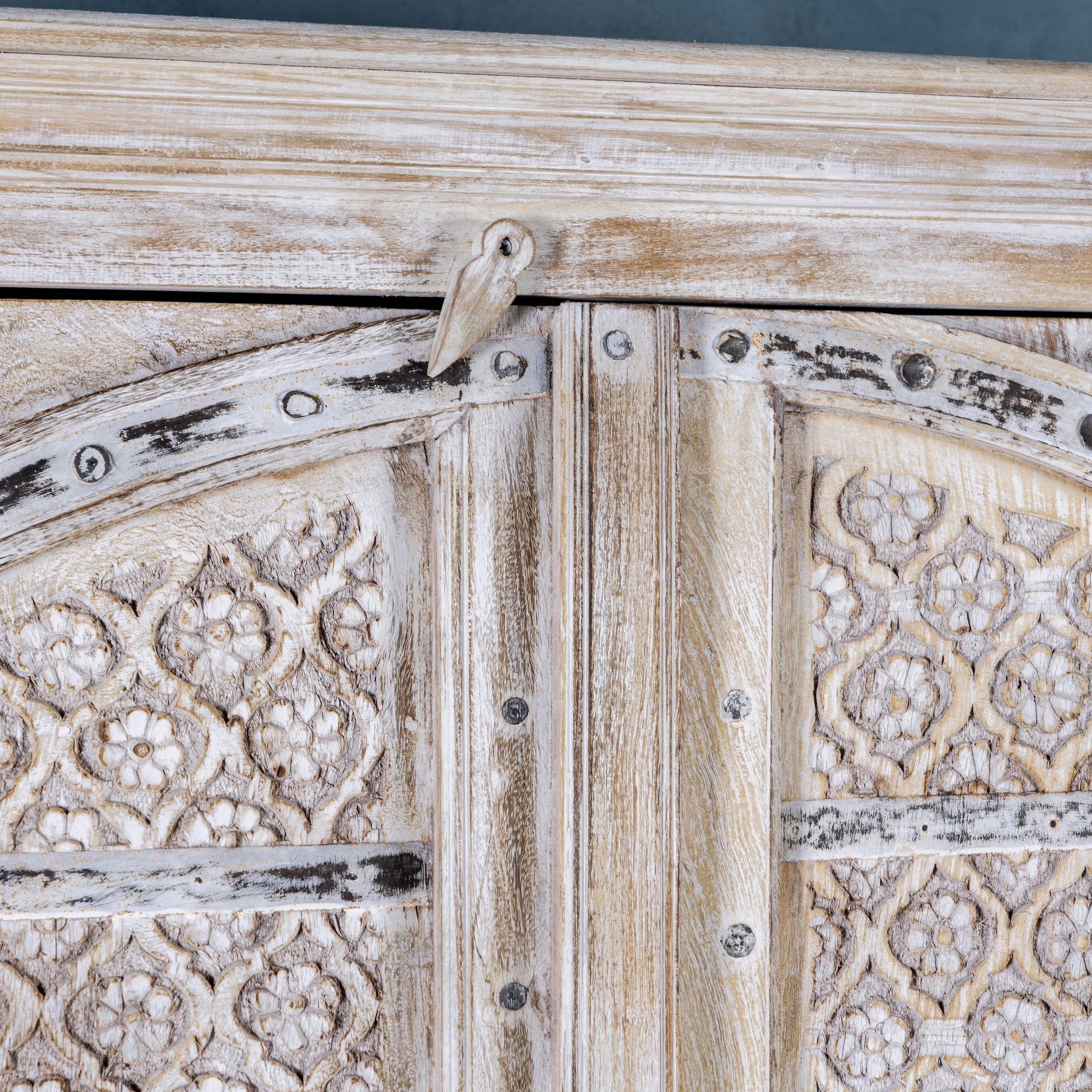 Close up picture of a cabinet made from an old teak door, featuring intricate hand-carved floral panels and a whitewashed finish- a striking piece with vintage charm and Ibiza style elegance.