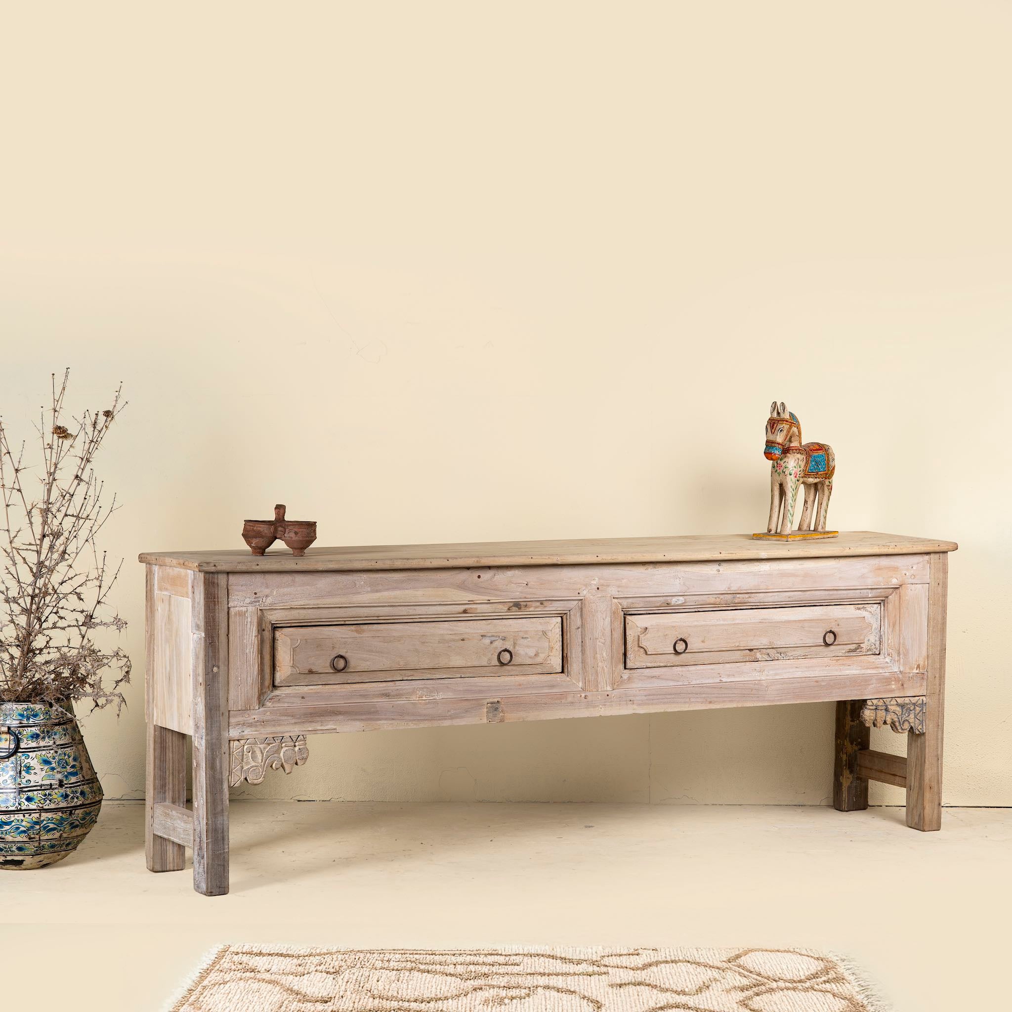 Side angle picture of a teak wood console table with two drawers, carved leg details, and sanded reclaimed finish, 223 × 45 × 83 cm.