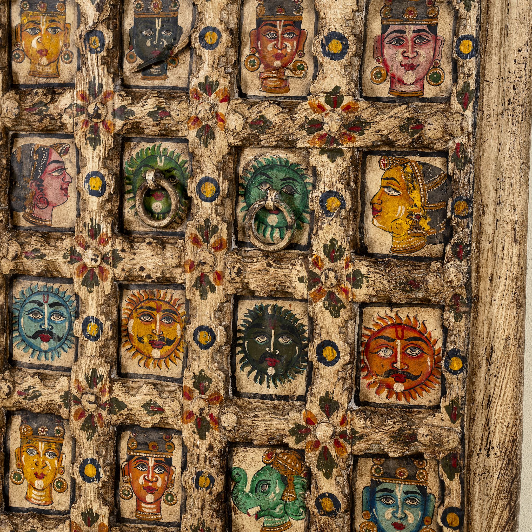 Close up image of a tall vintage wall panel made from reclaimed teak wood, intricately hand-painted with a grid of vibrant deity faces, animals, and symbolic motifs in rich colors, each framed within carved squares, reflecting traditional Indian folk art.