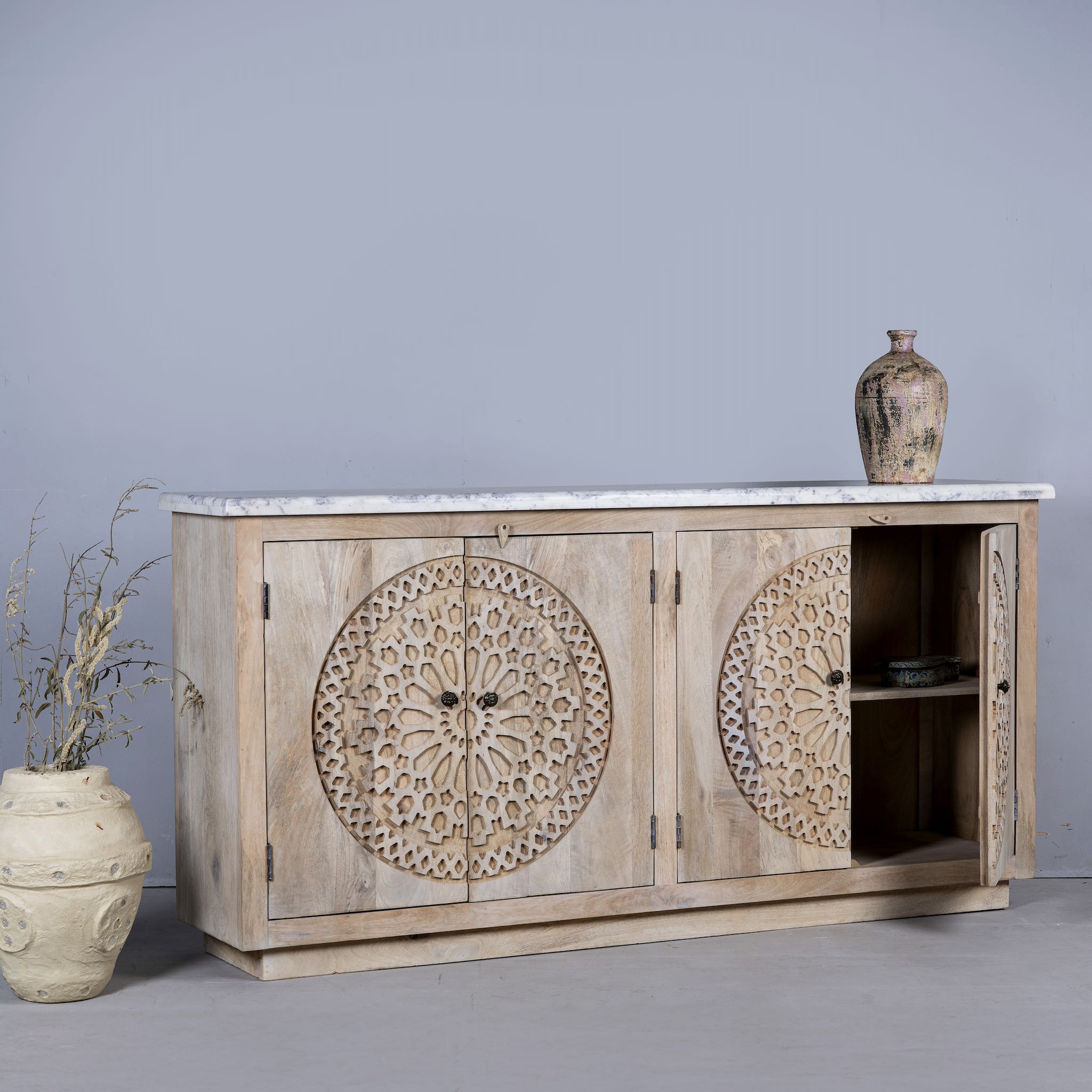 Open door view of a Acacia wood sideboard with circular carvings, 4 doors and iron handles with a white marble top.