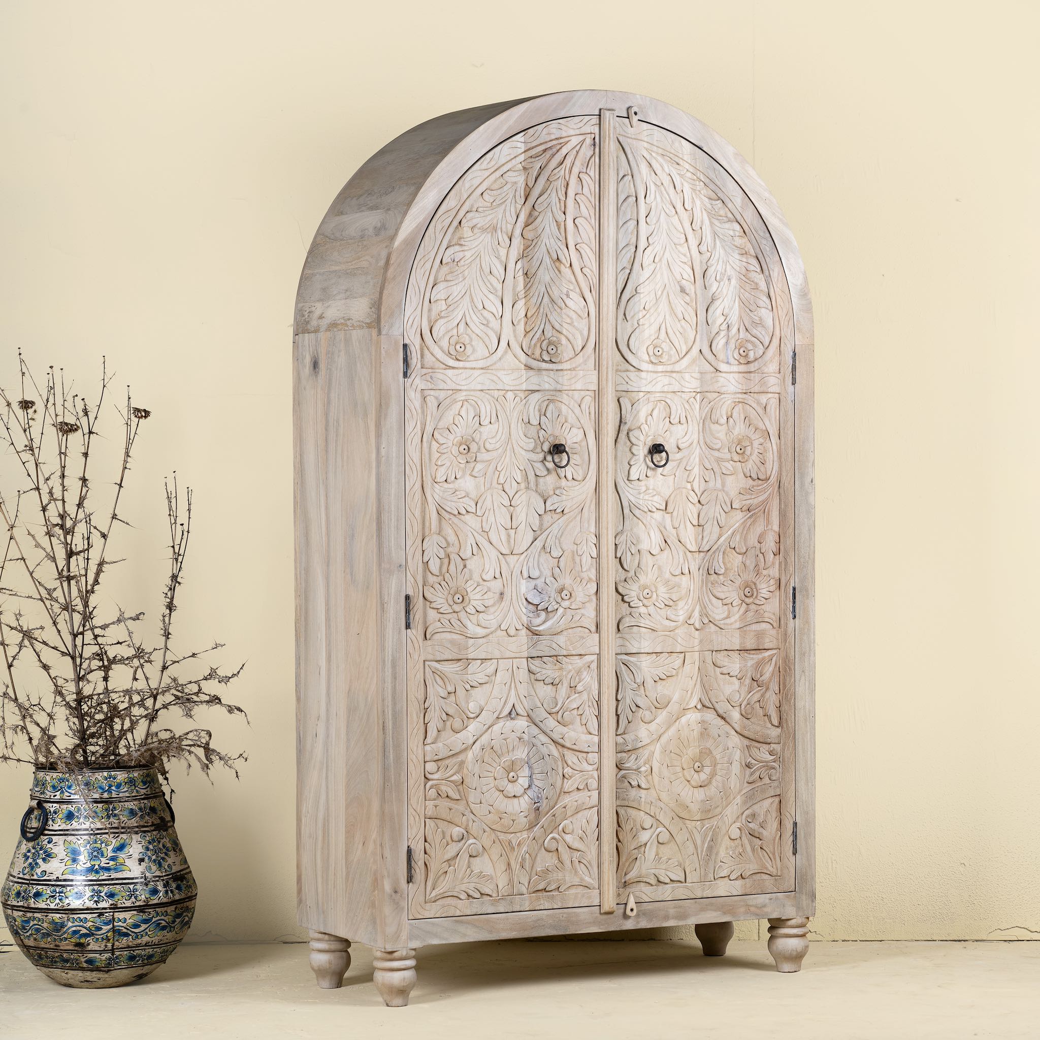 Side angle image of a handcrafted mango wood wardrobe with arched top and floral carving – Tamia by Om Home & Garden, unique furniture with Ibiza-style charm for living rooms and bedrooms.