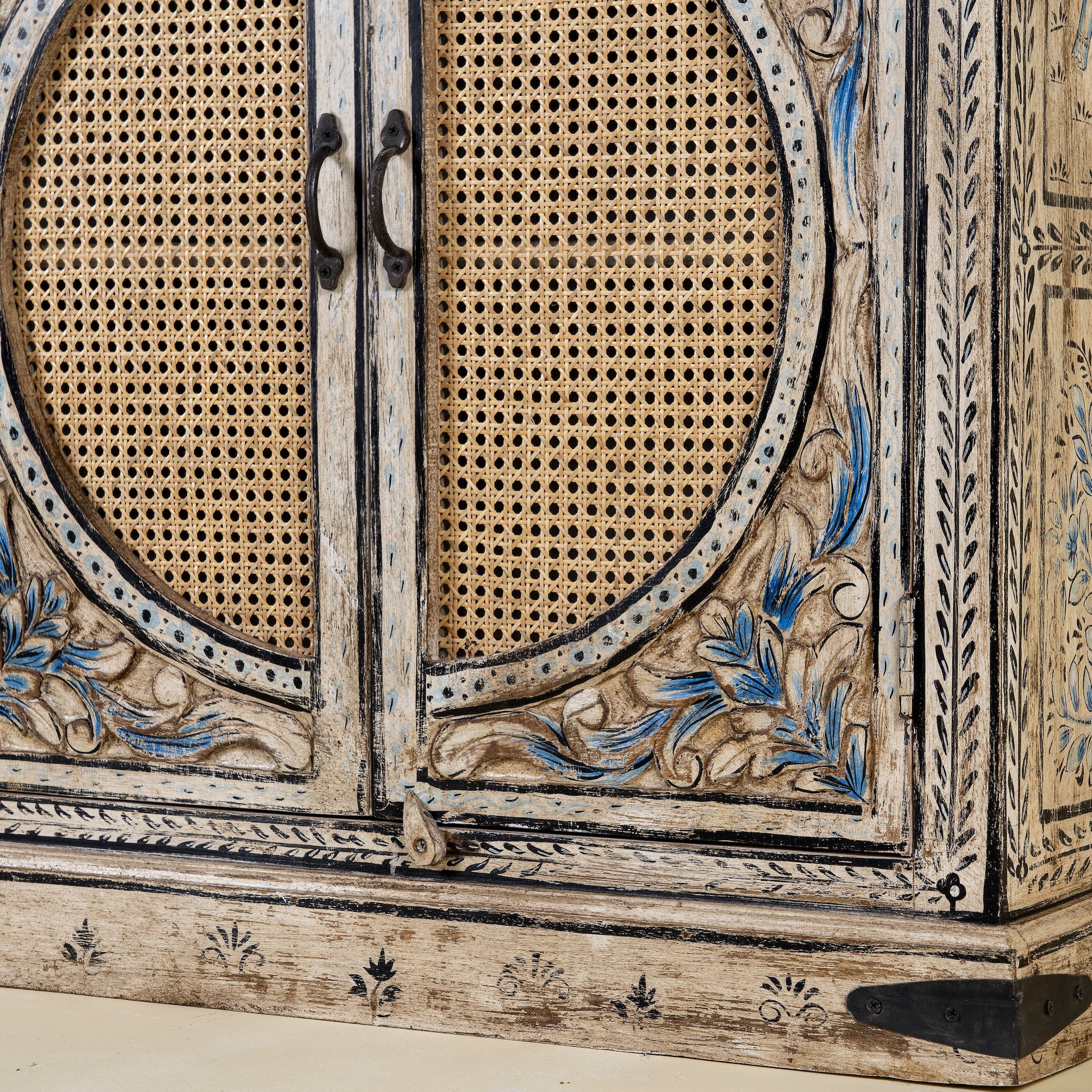 Close up view of a hand-made, hand-carved cupboard made of mango wood with blue floral designs, elephant motifs and rattan inserts.