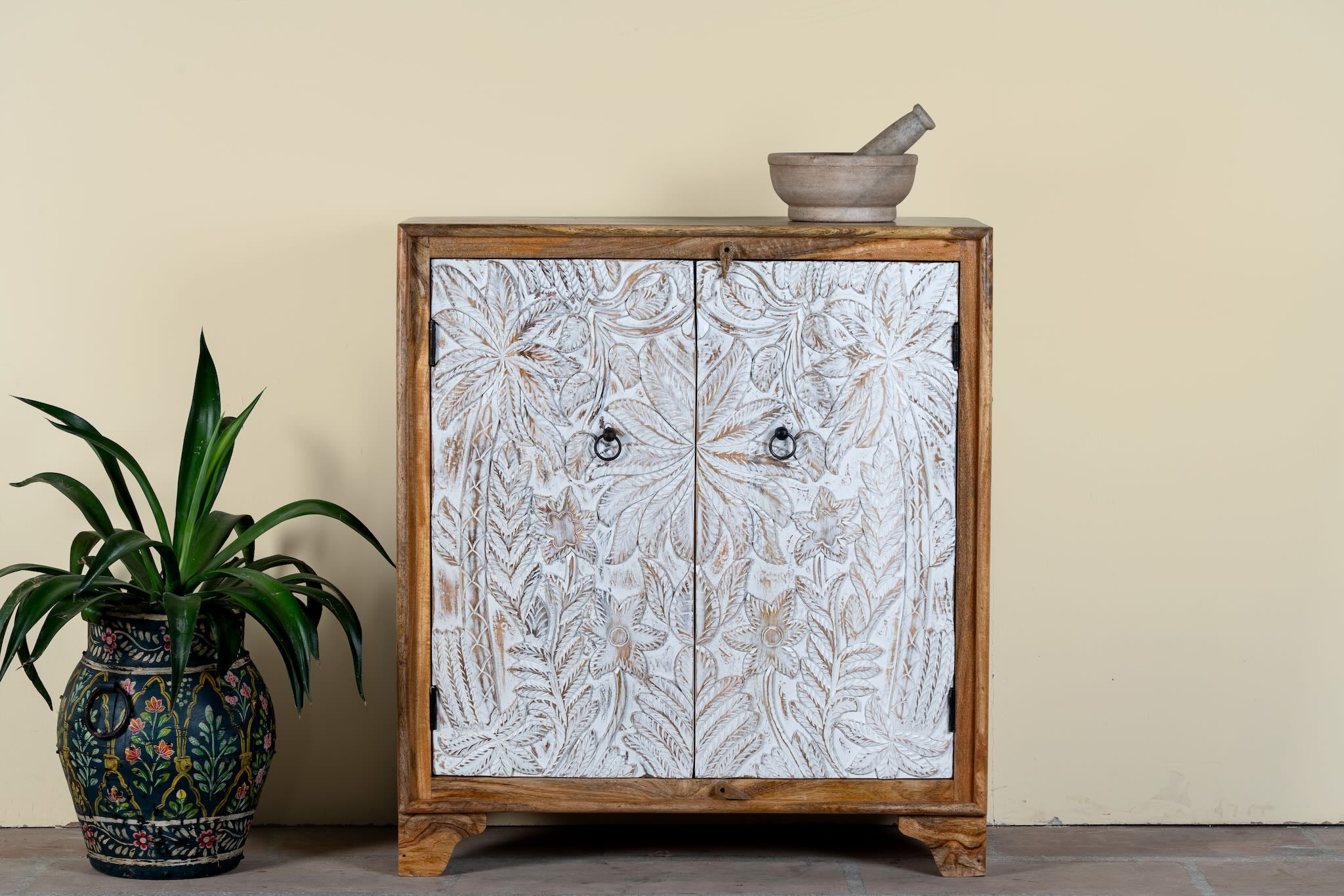 Hand-carved mango wood cupboard Utkarsh with whitewashed doors featuring palm tree and botanical motifs. A Mediterranean-inspired piece of Indian furniture combining artisan detail with practical storage.