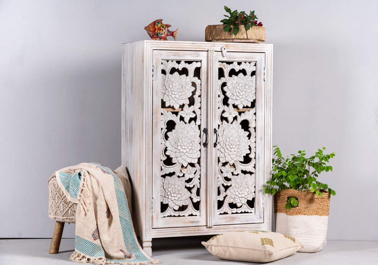 Side angle image of a white washed mango wood cabinet with three compartments and hand‑carved floral doors, vintage style, 75 × 40 × 120 cm.
