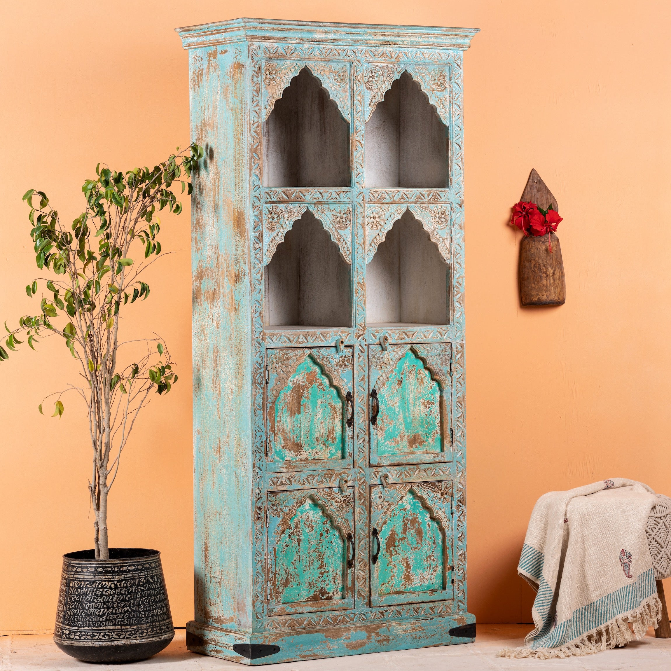 Side angle image of a hand-carved mango wood shelf with arched open display and lower cabinets – vintage home decoration piece in distressed pastel blue finish with Indian architectural detailing.