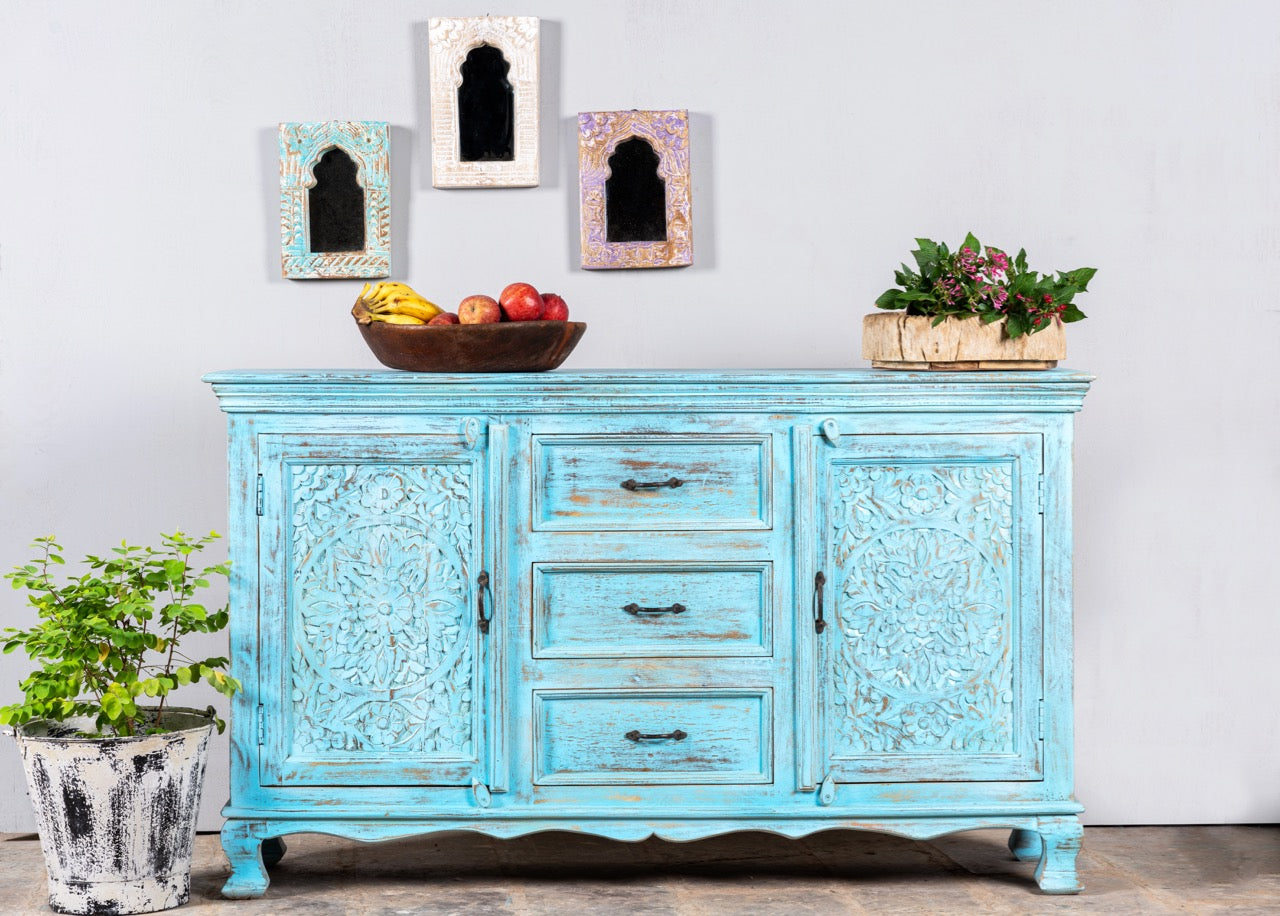 Lifestle image of a hand-carved mango wood sideboard with distressed blue wash finish, artisanal furniture for bohemian interior, 150 × 40 × 90 cm.