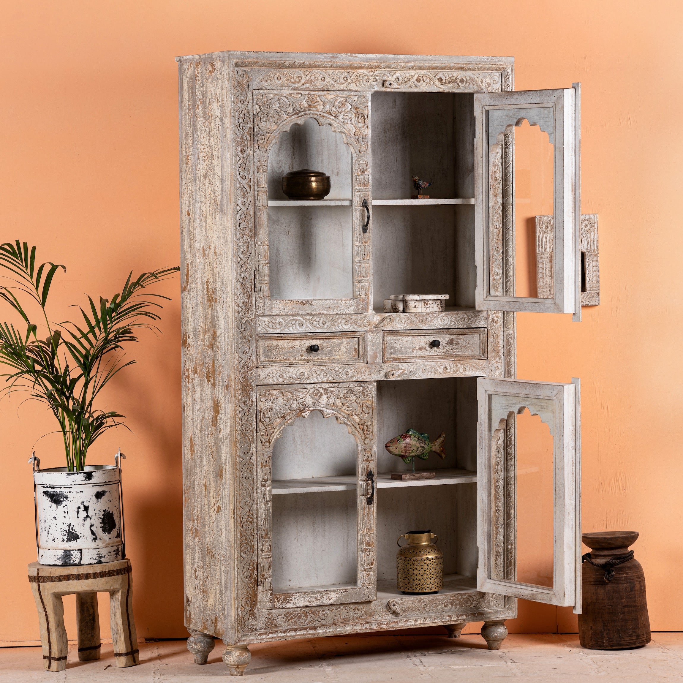 Side angle image with open door of a hand-carved mango wood showcase with glass doors and drawers – carved wooden furniture in distressed turquoise and blue, combining artisan detail with vintage charm.