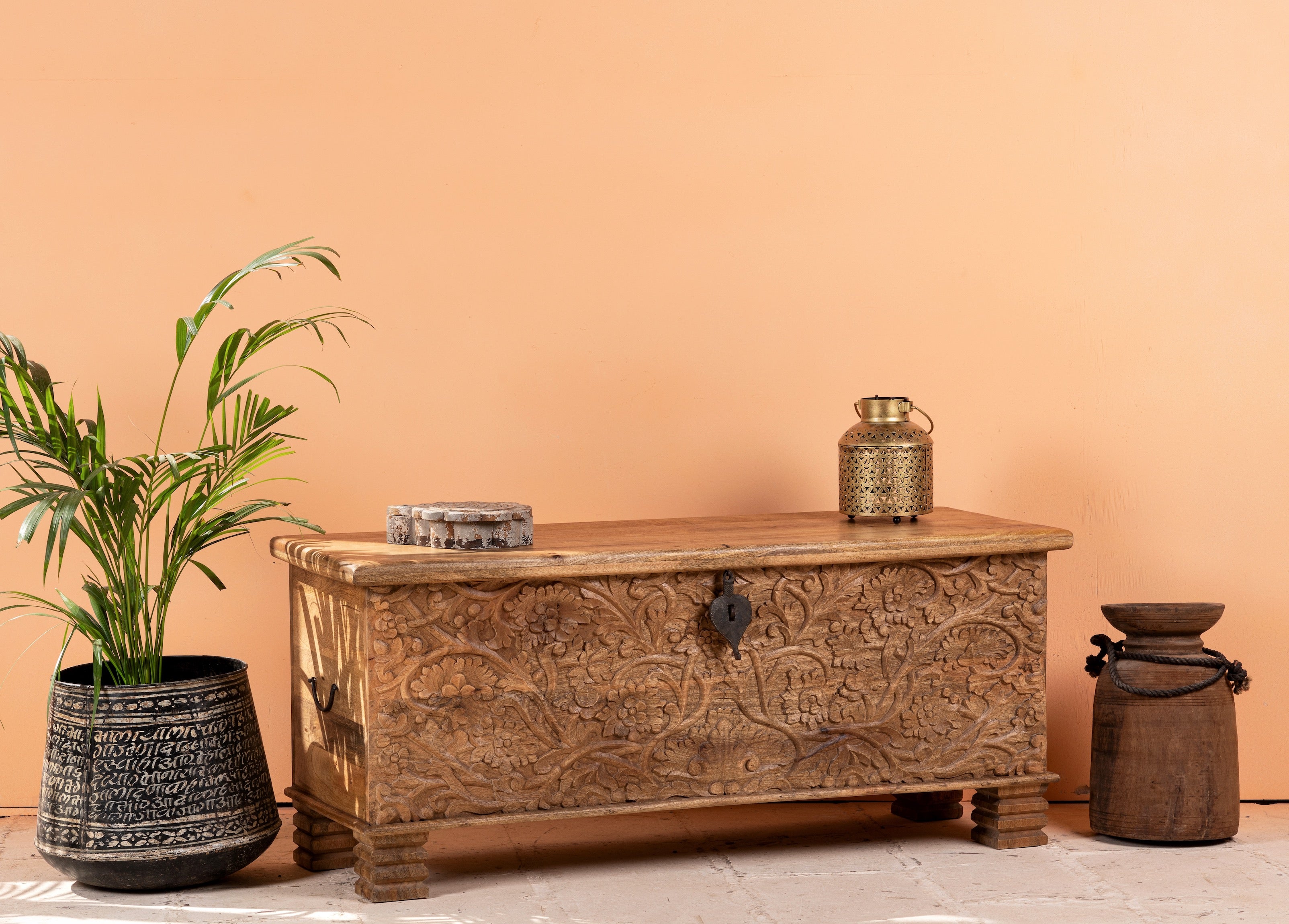 Side angle image of a hand-carved mango wood storage chest with floral detailing and iron fittings – wooden carved chest ideal for use as elegant bedroom furniture or storage.