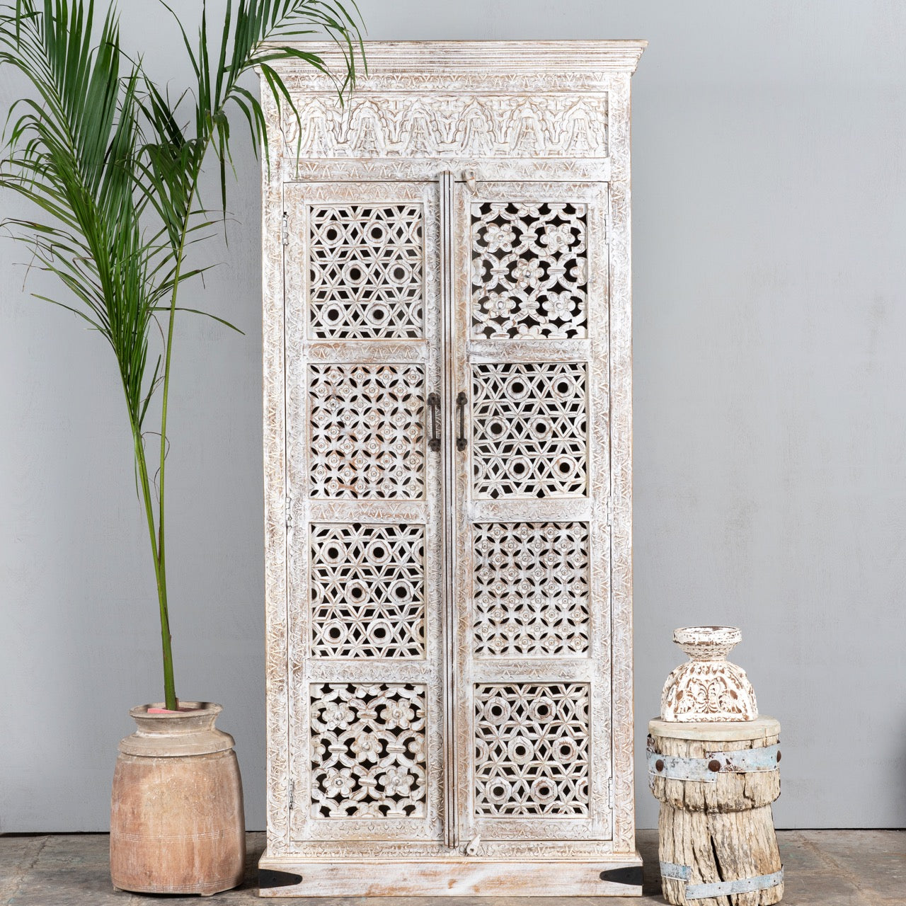Lifestyle image of a hand-carved mango wood wardrobe with whitewashed finish, bedroom furniture wooden wardrobe with floral and geometric lattice doors, 90 × 190 × 40 cm.